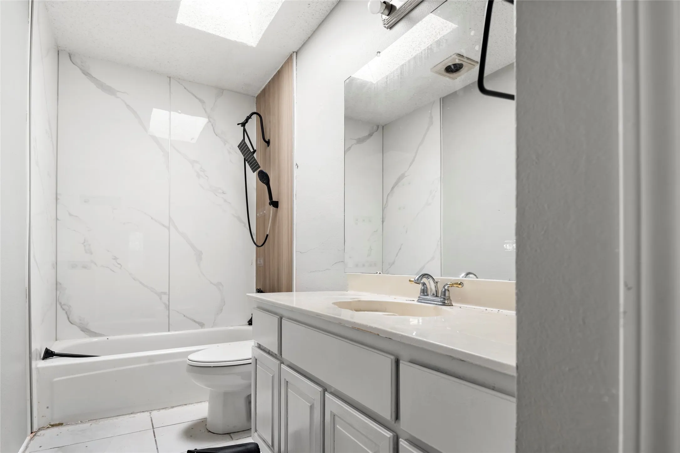 Full bathroom featuring a white bathtub with a tile surround, a skylight, and a vanity with an integrated sink and base cabinetry