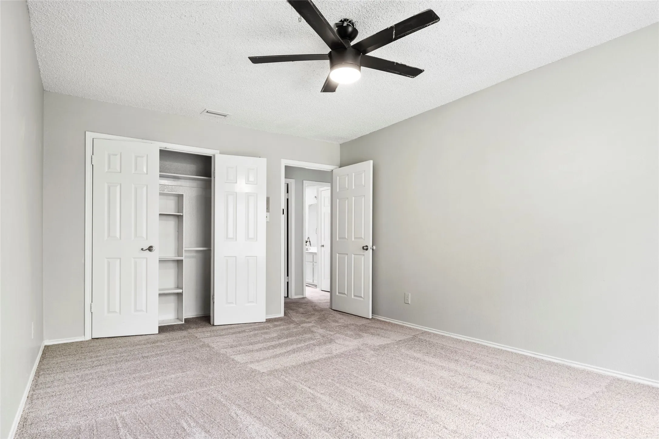 Spacious room featuring neutral paint tones, light-toned carpet flooring, a ceiling fan with integrated lighting, and a built-in closet with shelving and hanging rods