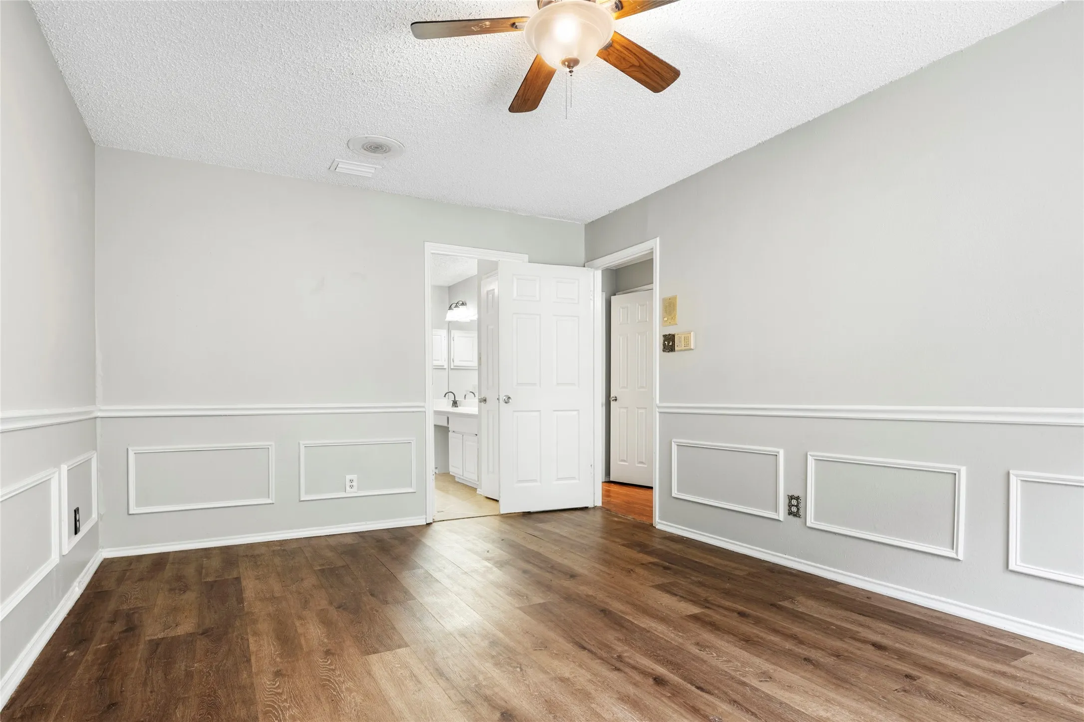 Spacious interior featuring wood-finish flooring, wainscoting, and a ceiling fan