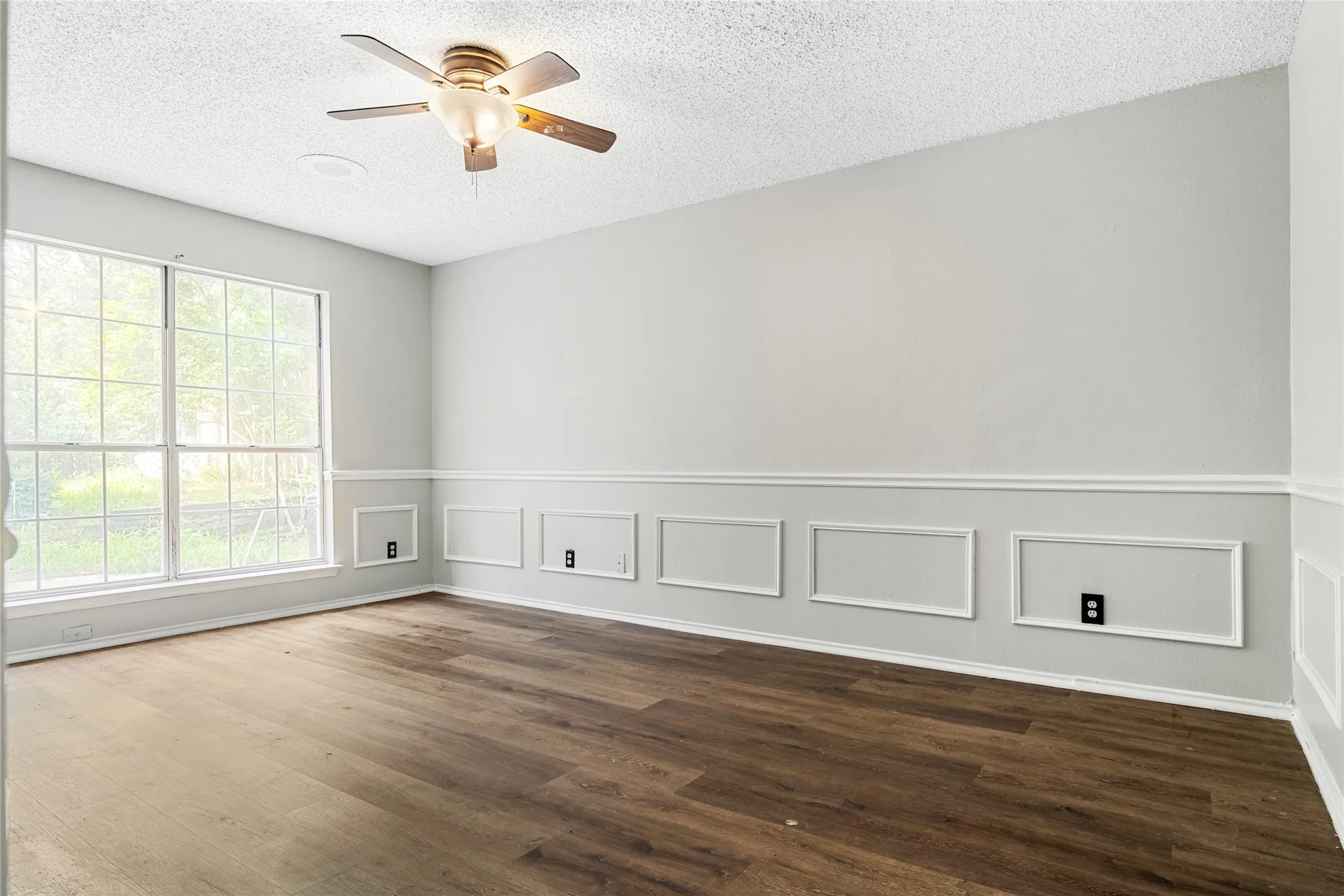 Spacious interior featuring wood-finish flooring, a multi-paned window, and a ceiling fan with integrated lighting