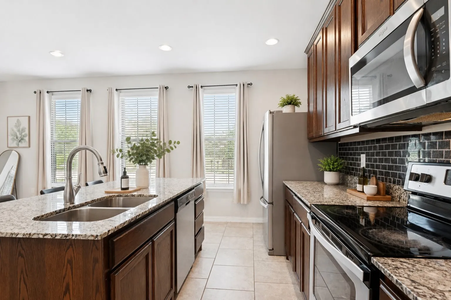 Kitchen featuring an expansive island with a double basin sink, stainless steel appliances, dark wood cabinetry, granite countertops, and tile flooring
