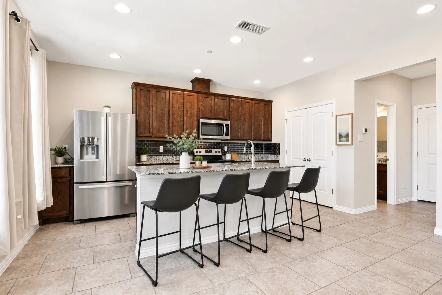 Open-concept kitchen featuring an island with a breakfast bar, stainless steel appliances, wood cabinetry, stone countertops, and tile backsplash