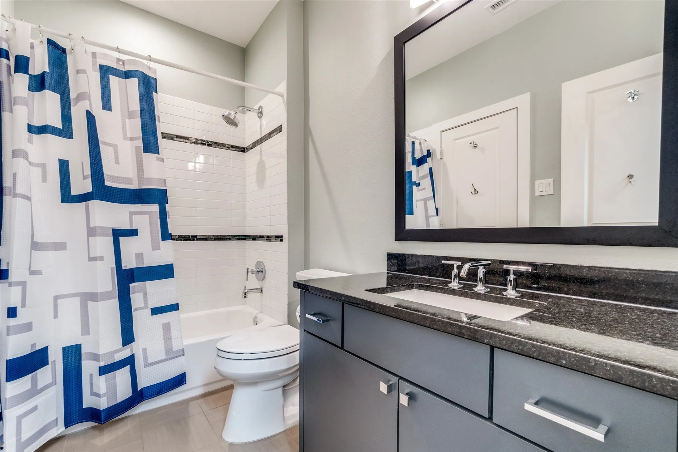 Bathroom featuring a white subway tile shower surround with decorative accent bands, a white bathtub, and a built-in vanity with a dark stone countertop and undermount sink