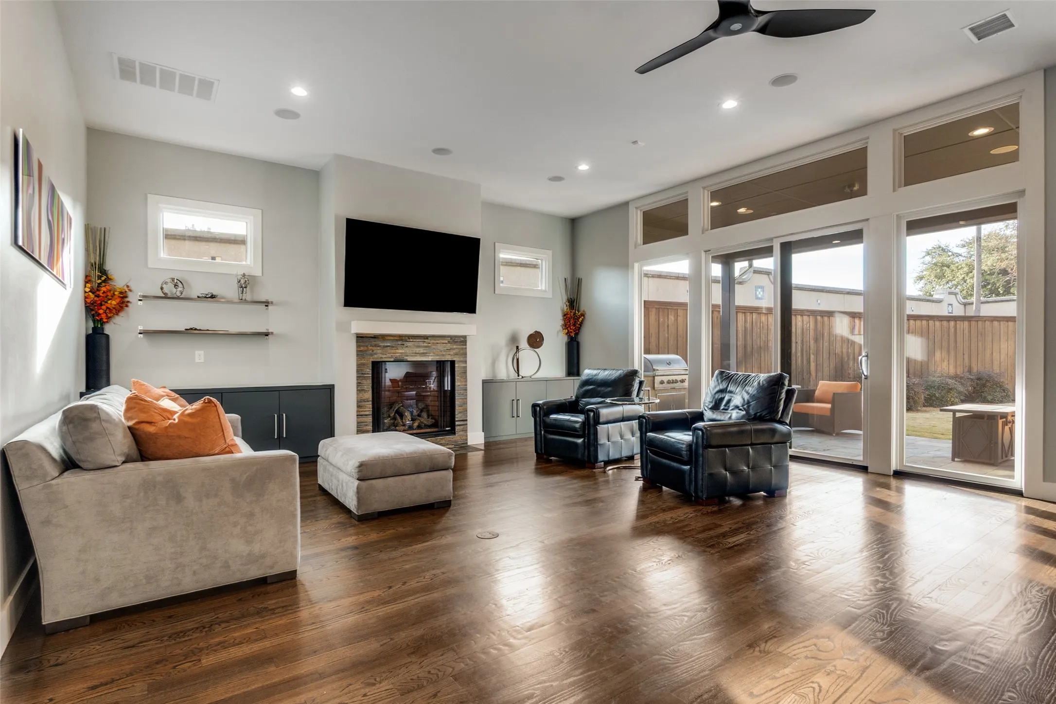 Spacious living area featuring rich wood-finish flooring, a contemporary fireplace with stacked stone surround, and extensive glass sliding doors