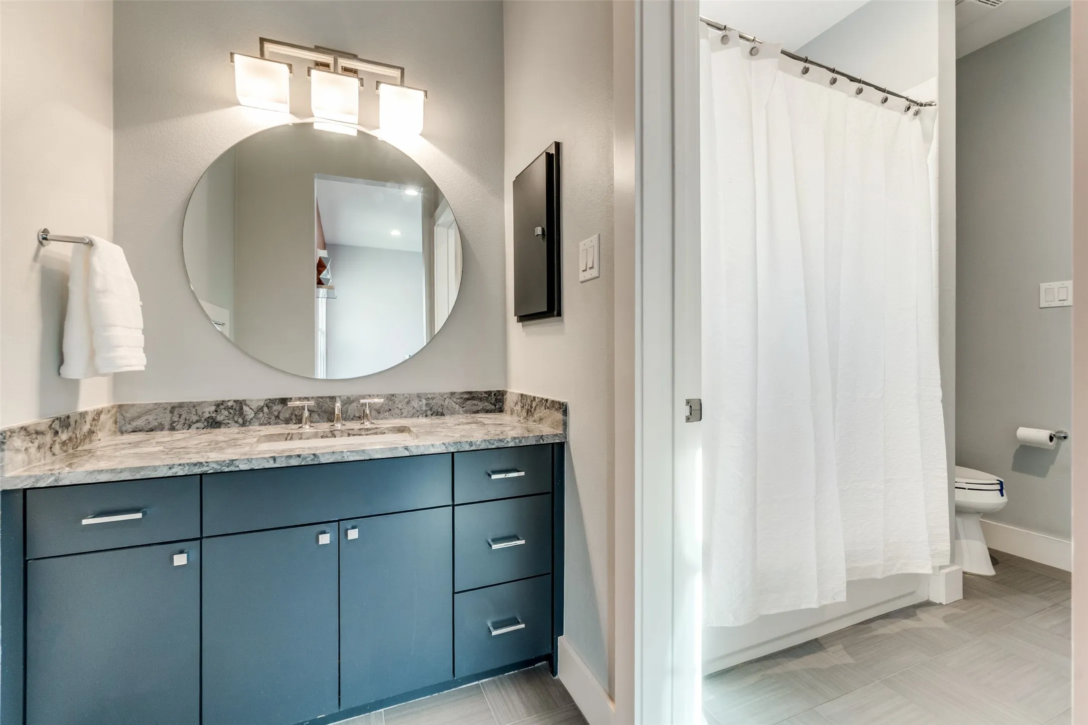 Contemporary bathroom vanity featuring a circular mirror, modern light fixture, polished countertop, and ample storage cabinetry