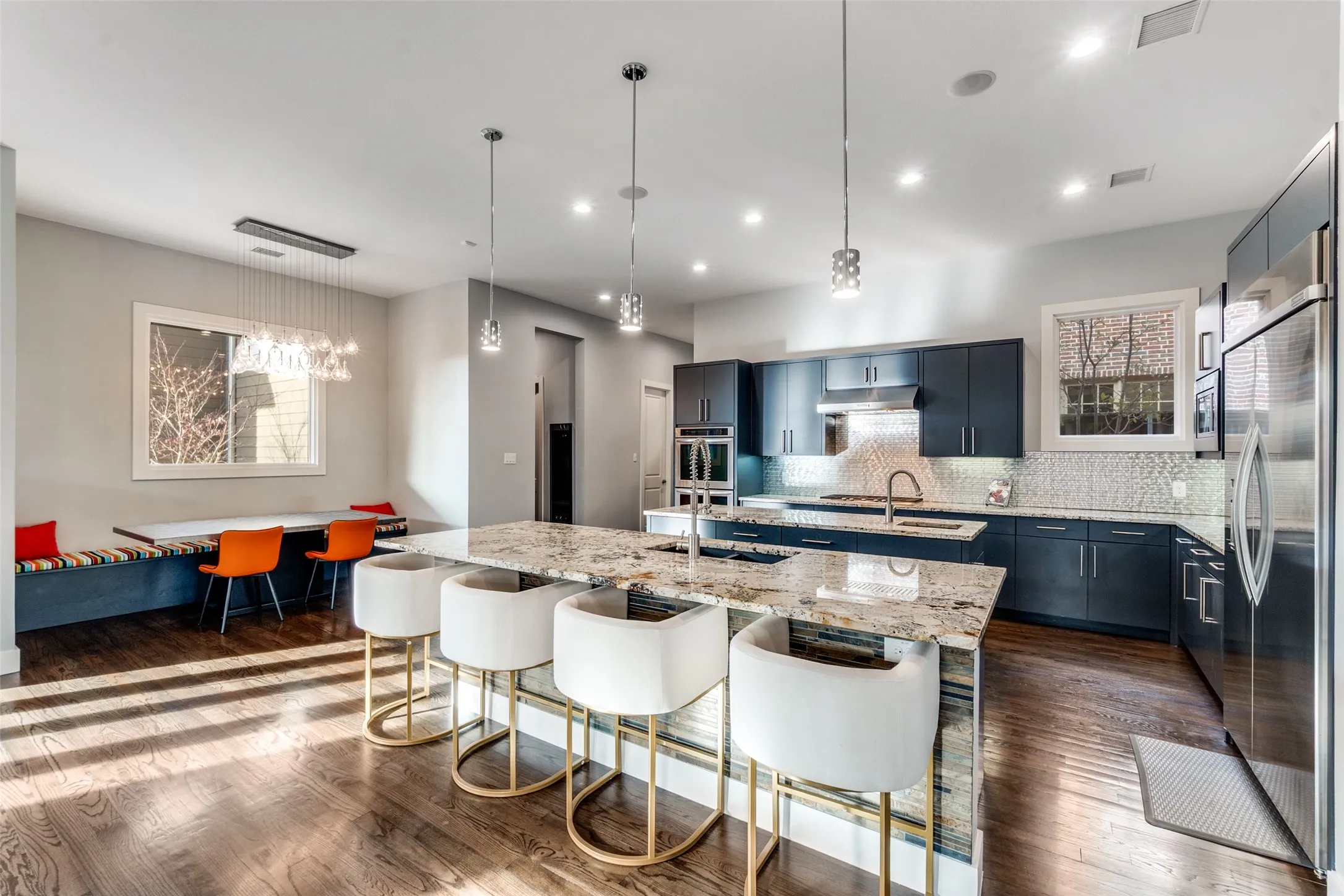 Spacious kitchen featuring dark cabinetry, stainless steel appliances, a large center island with a granite countertop, and wood-finish flooring throughout