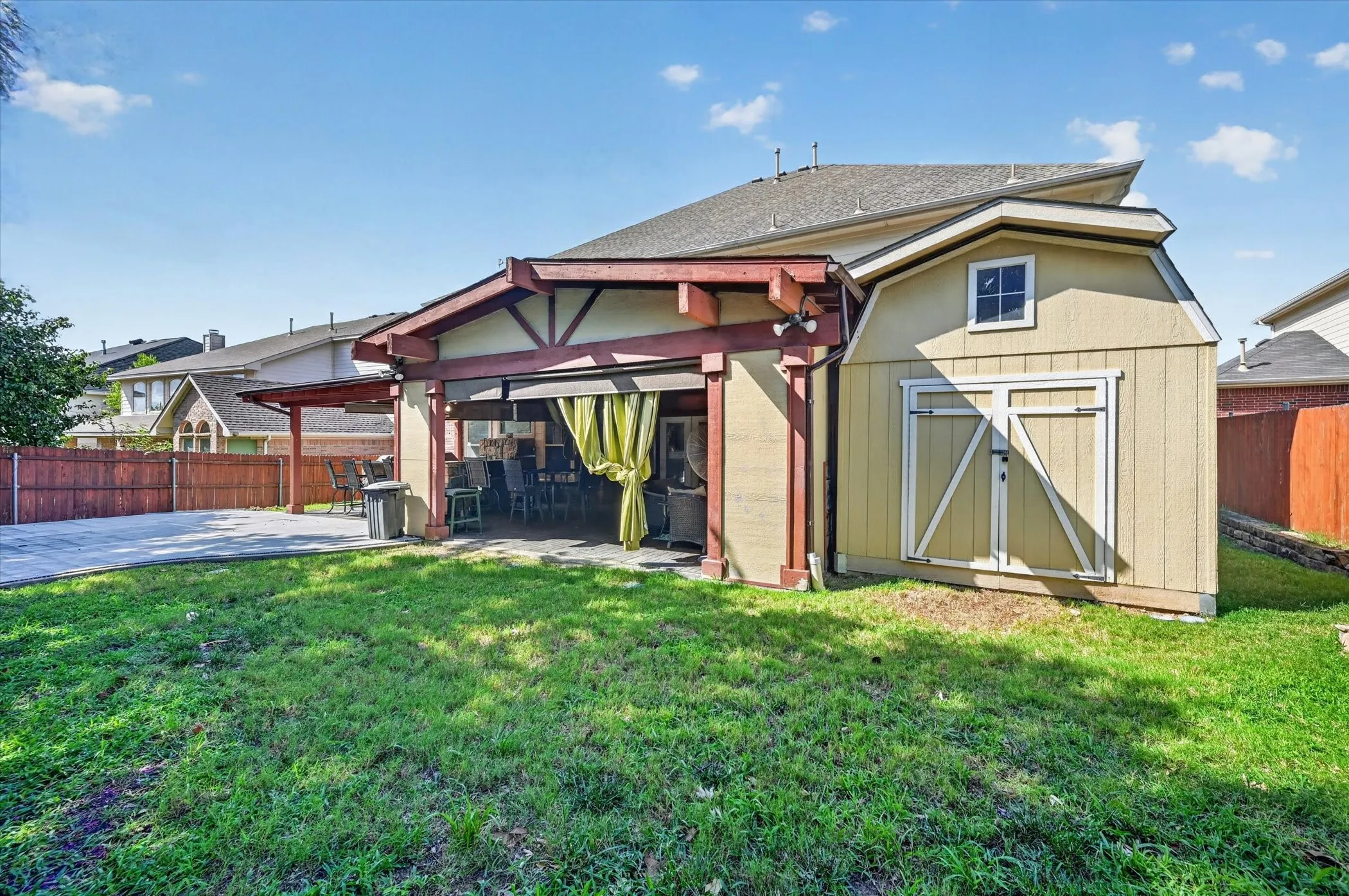 Expansive backyard featuring a covered patio with exposed beam details, a detached storage shed, a paved patio area, and a privacy fence