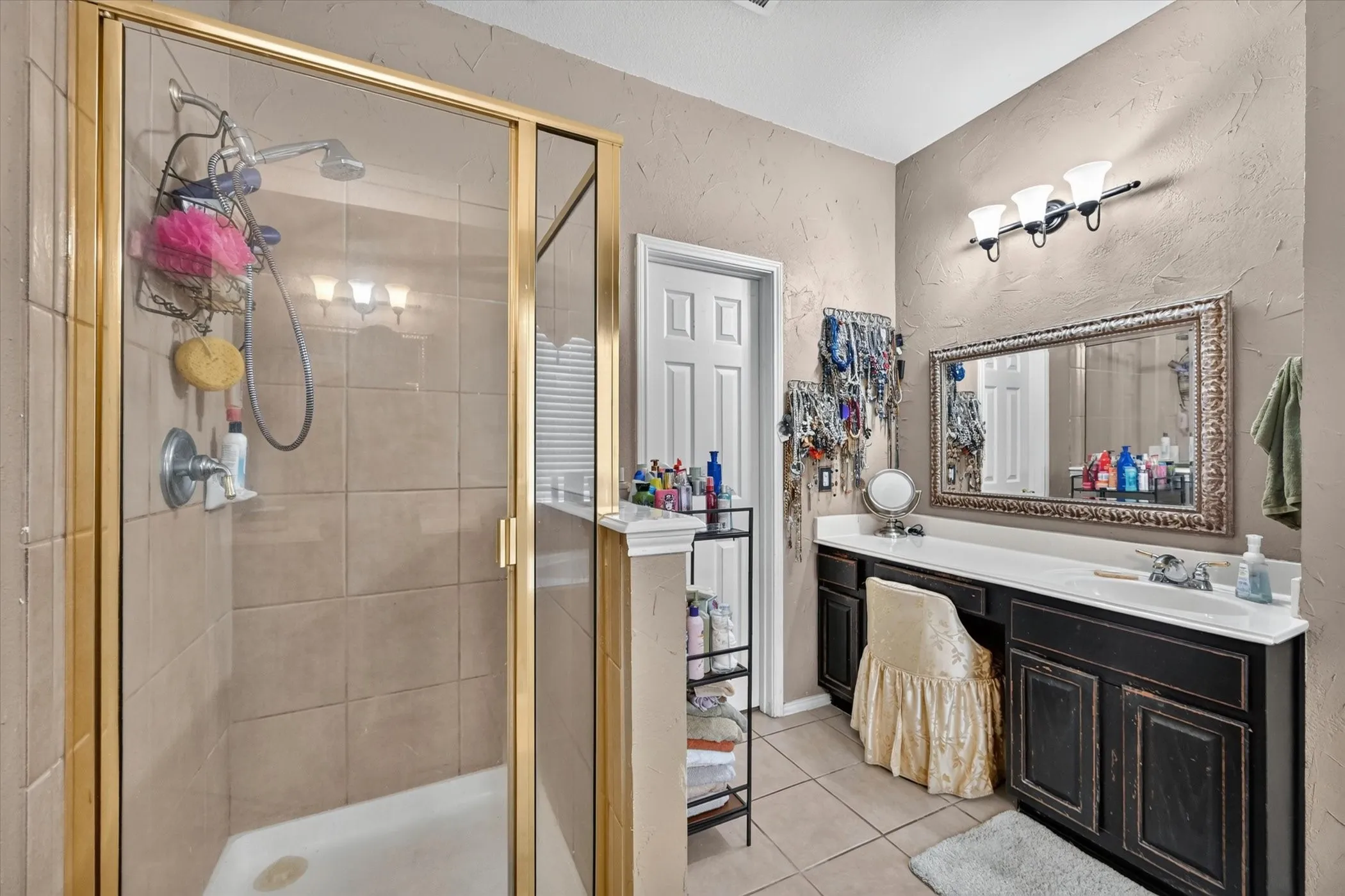 Bathroom featuring a glass-enclosed shower with gold-tone hardware, a single vanity with integrated sink, a large framed mirror, and a three-light vanity fixture