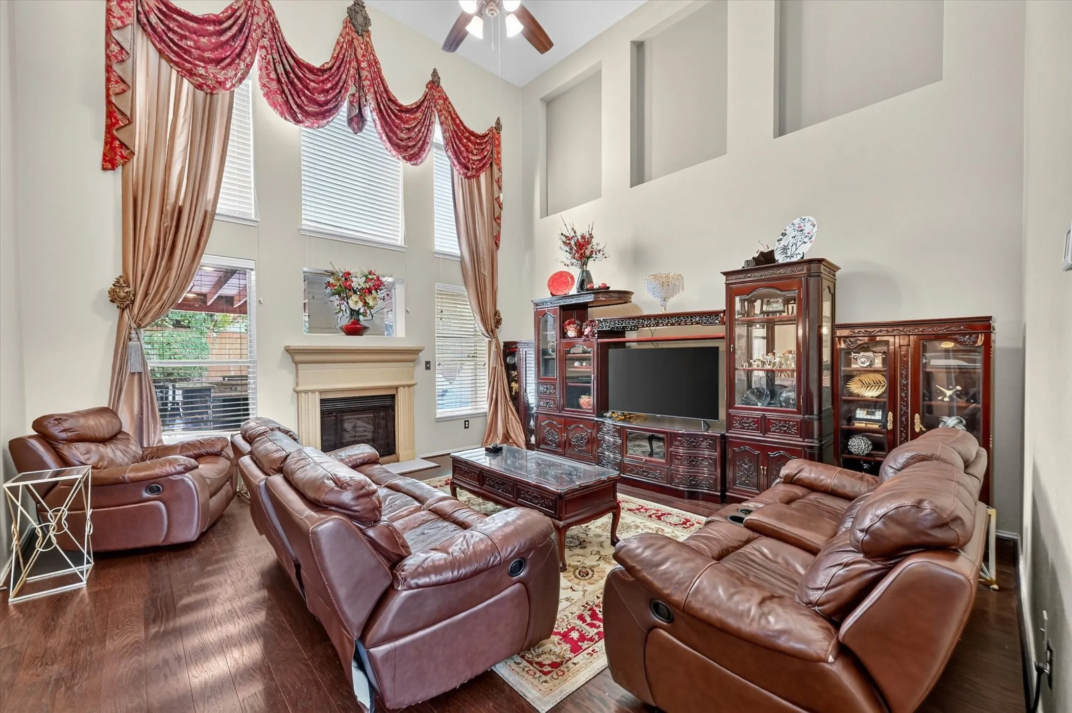 Living area featuring high ceilings, wood-finish flooring, a ceiling fan, and multiple windows with blinds