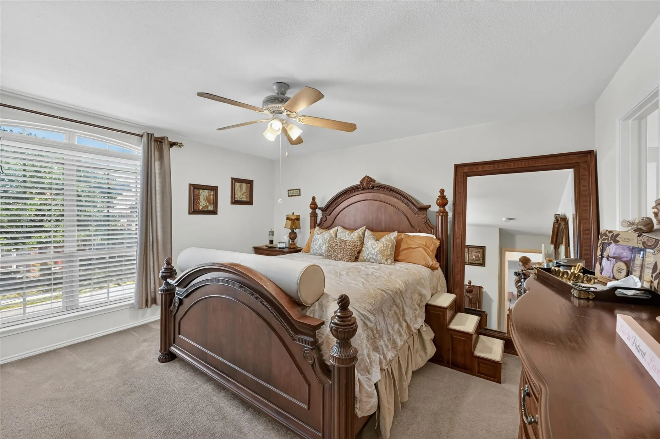 Carpeted bedroom featuring a large window with horizontal blinds, a ceiling fan with integrated lighting, and white walls