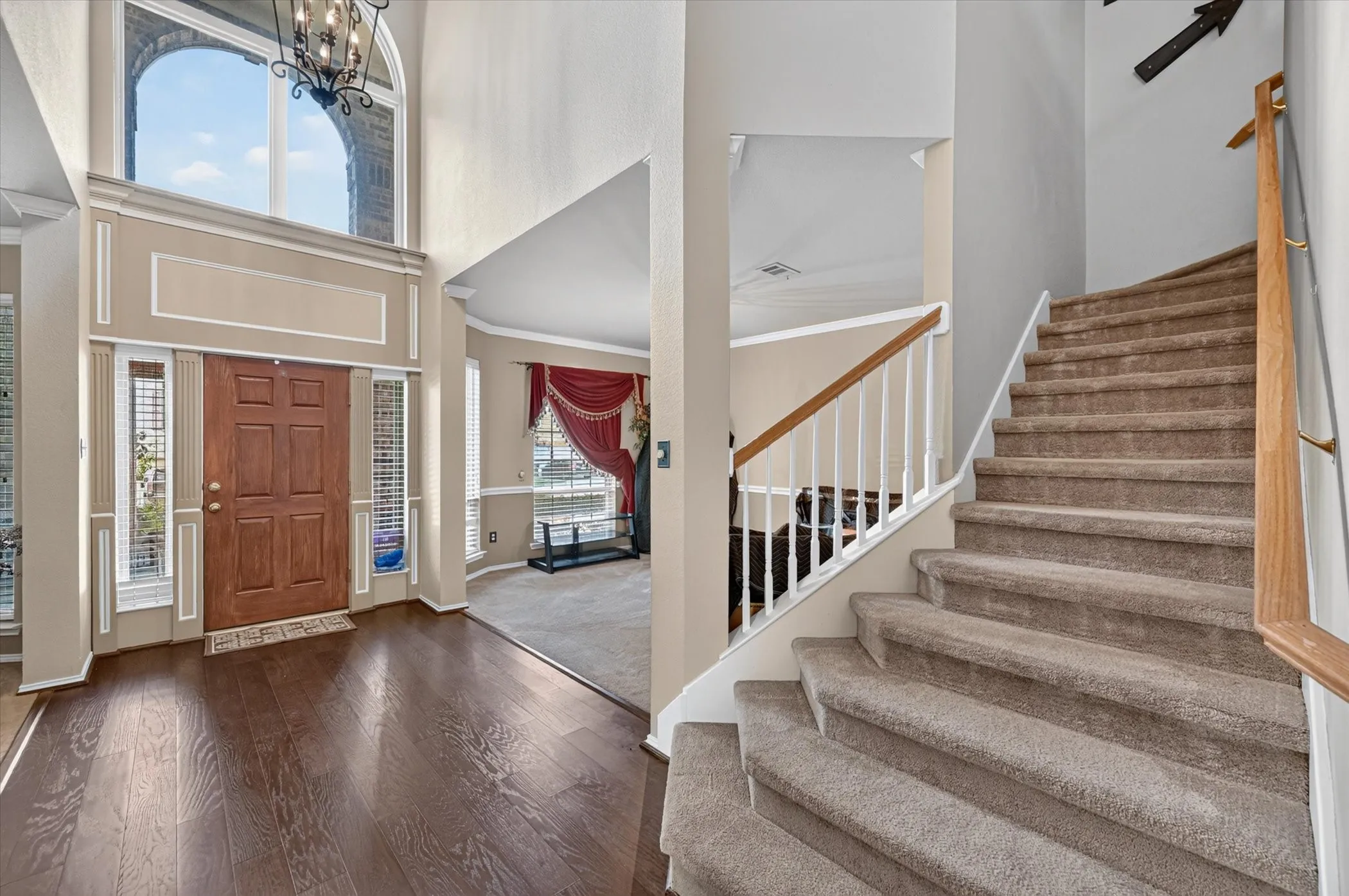Two-story foyer with a dark wood-finish flooring, a grand arched window, and a chandelier