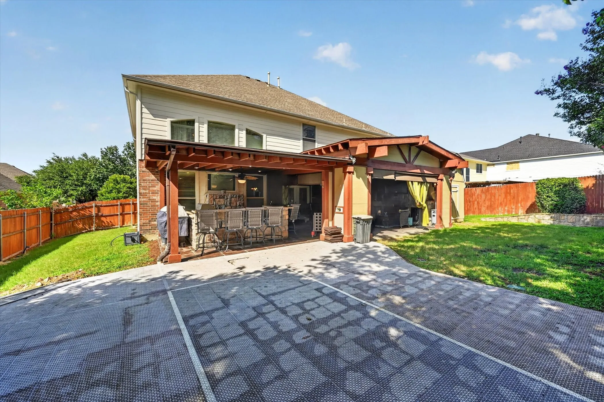 Rear exterior featuring a covered outdoor kitchen with stone accents, a second covered patio area, and a patterned hardscape surface