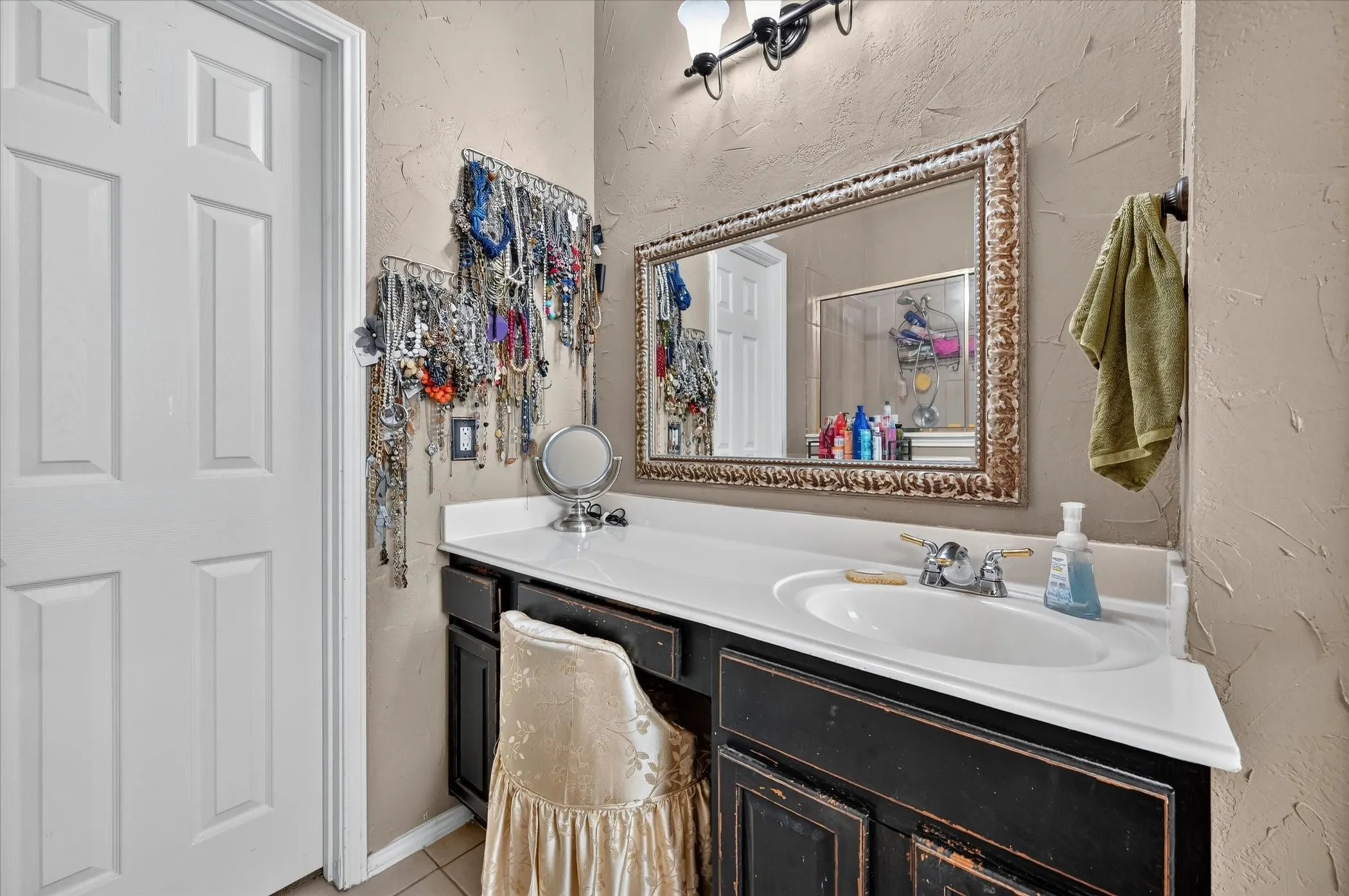 Vanity area featuring a distressed black wood-finish cabinet with a built-in sink, white countertop, and an ornate framed mirror