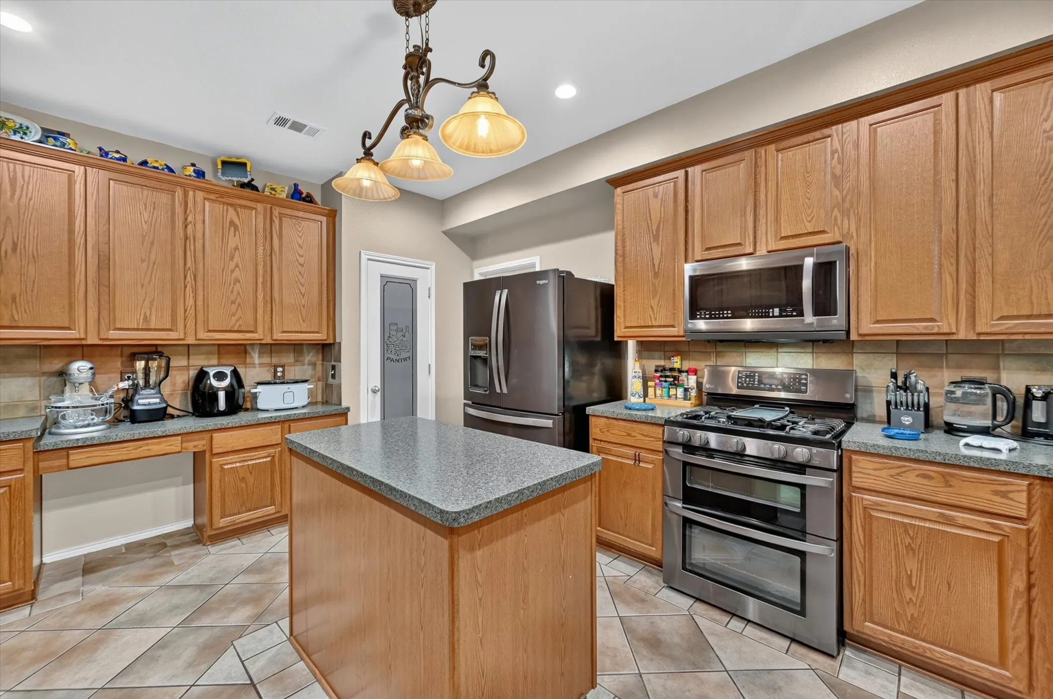 Kitchen featuring wood cabinetry, stainless steel appliances, a central island with a speckled countertop, and a tiled floor