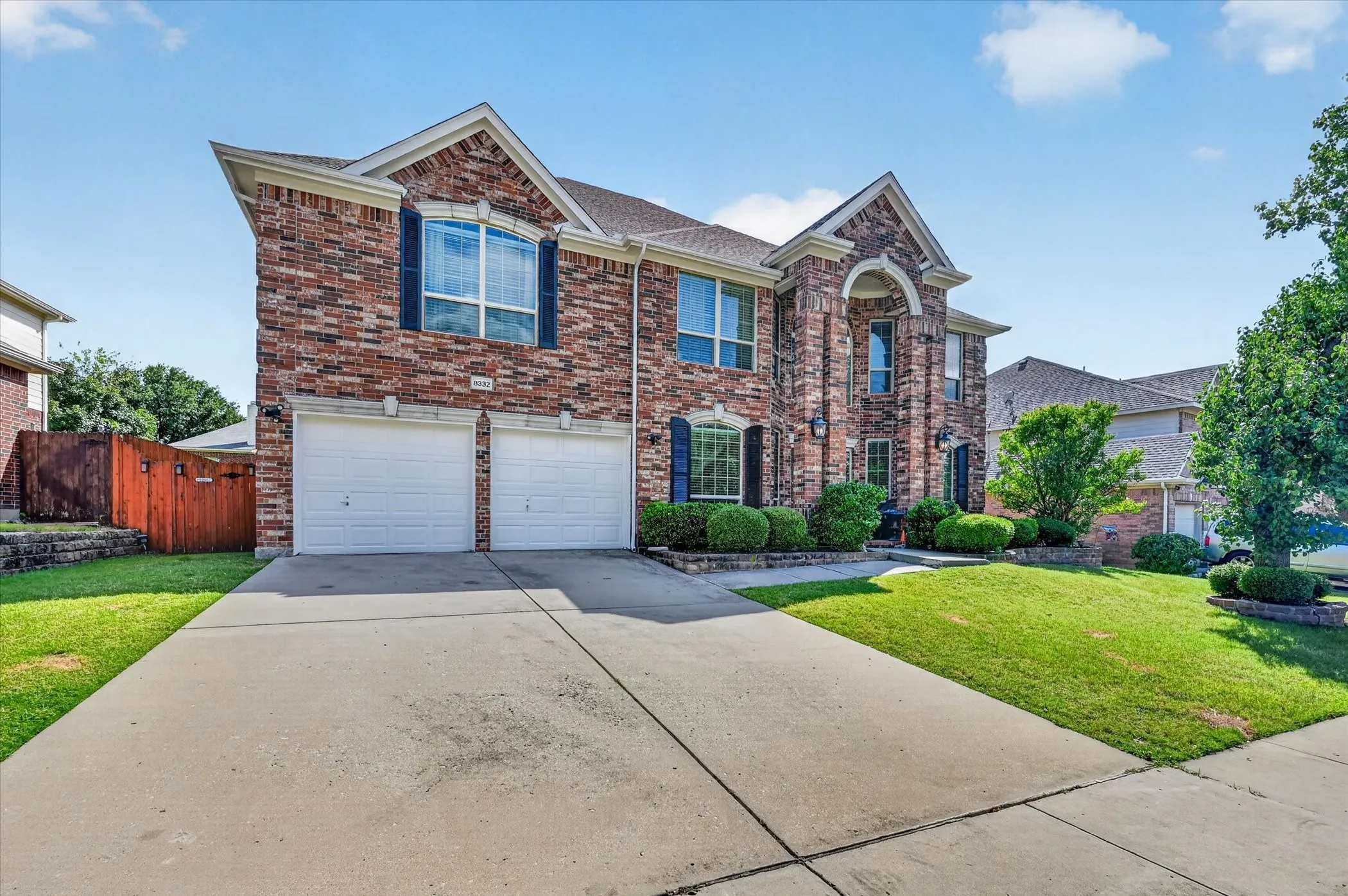 Brick facade residence with a dual garage, arched entryway, and mature landscaping