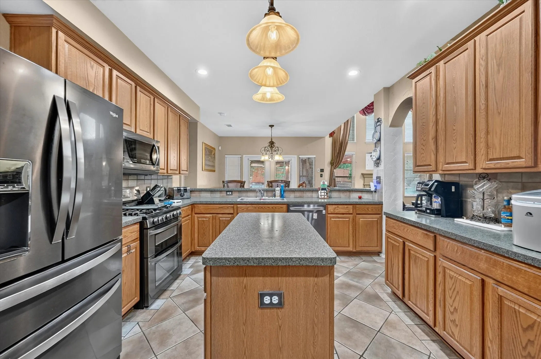 Kitchen featuring a central island with a stone-finish countertop, abundant wood cabinetry, stainless steel appliances, and tiled flooring
