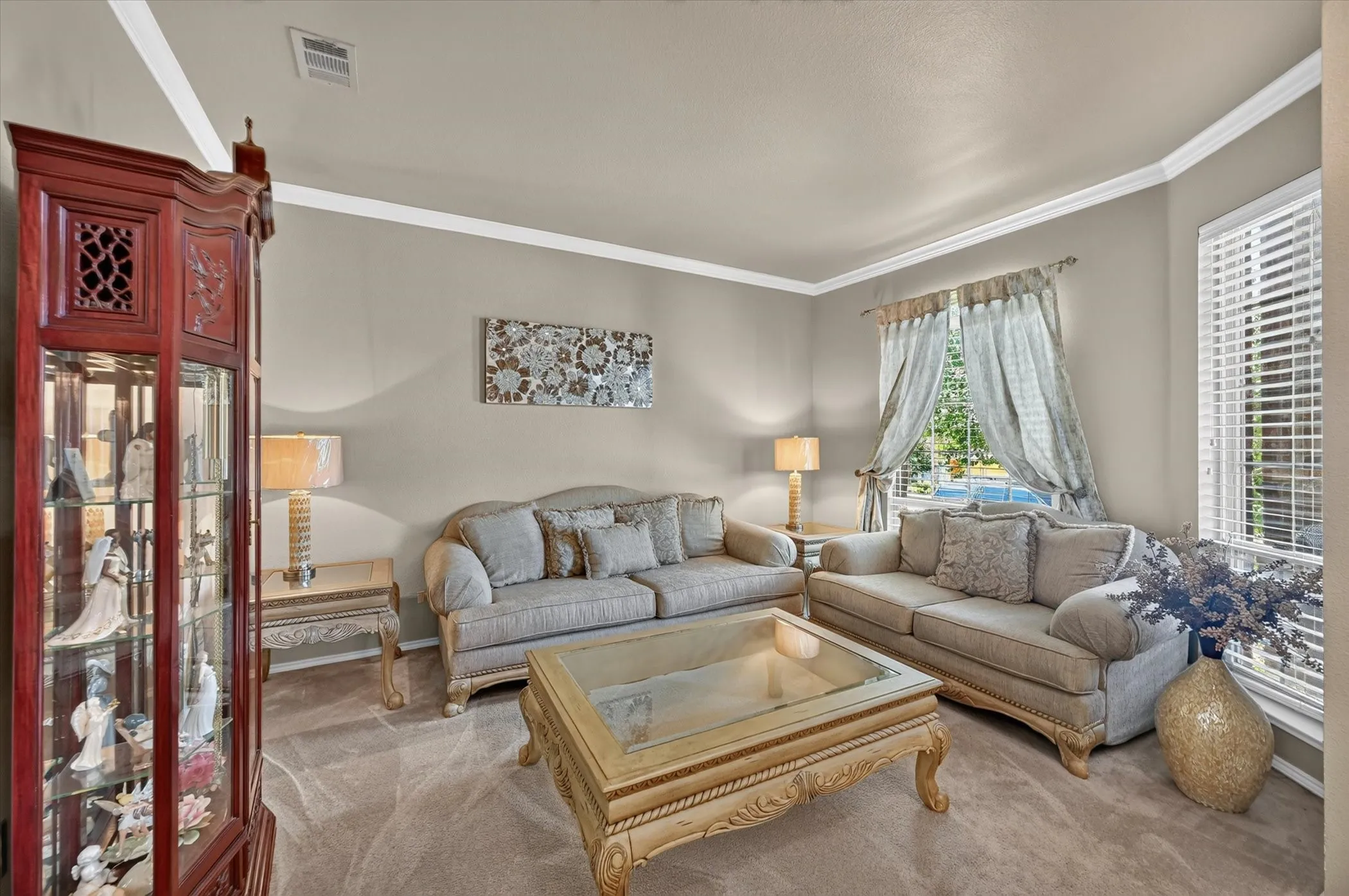 Living area featuring neutral-toned walls with crown molding, carpeted flooring, and a large window with blinds