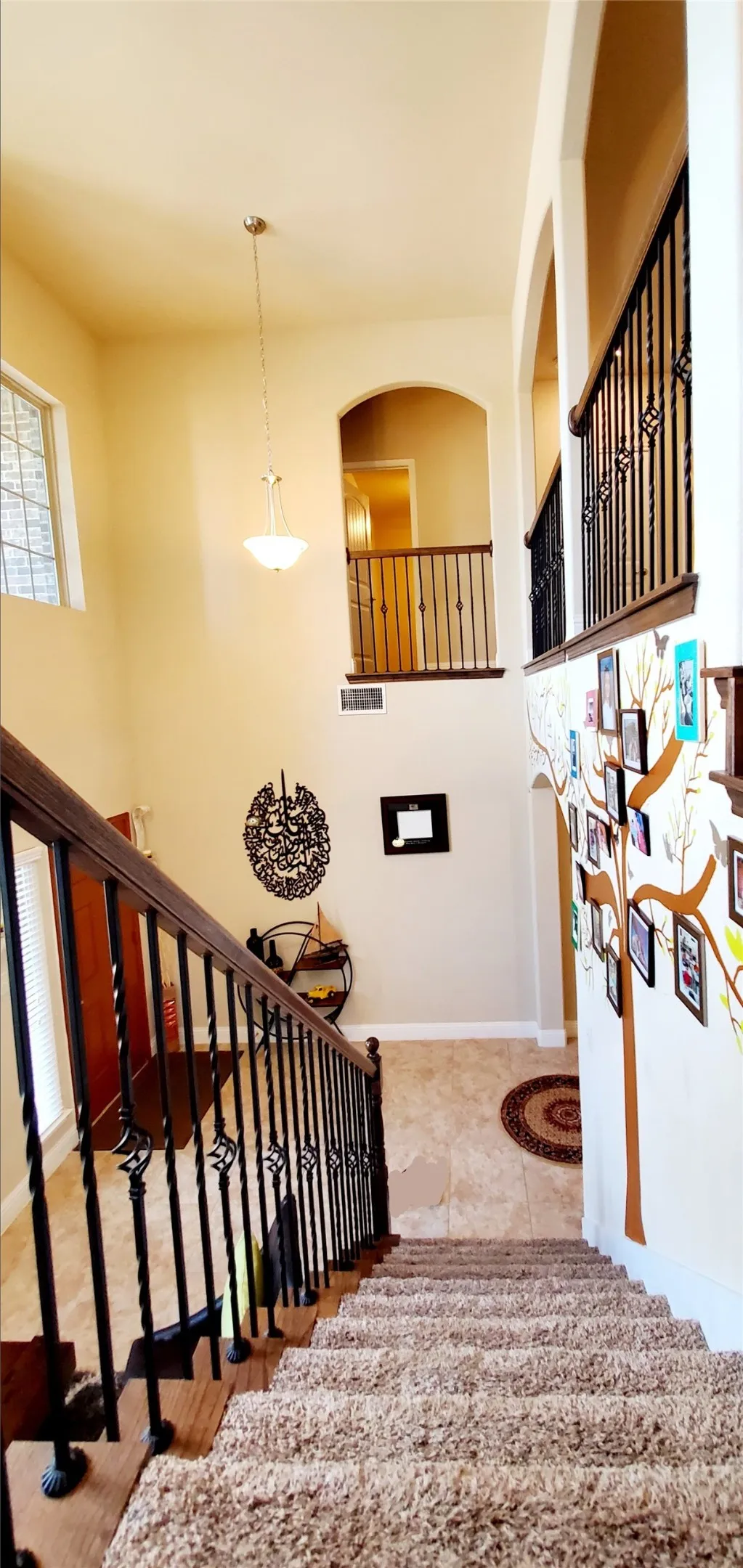 Two-story entry featuring a carpeted staircase with wrought iron balusters, wood handrails, and a stained glass window