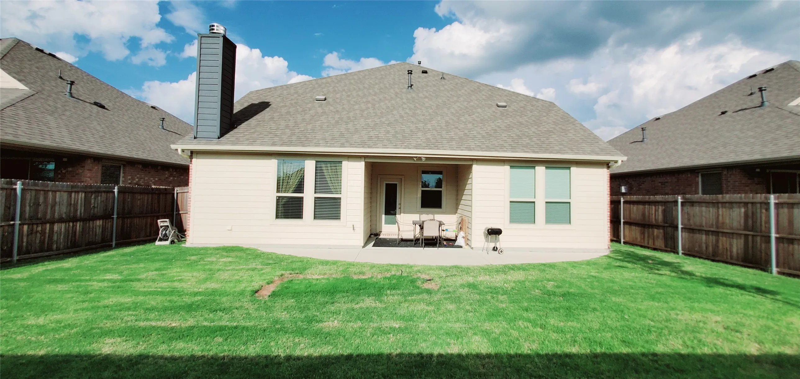 Expansive rear yard featuring a concrete patio, a full privacy fence, and a modern chimney