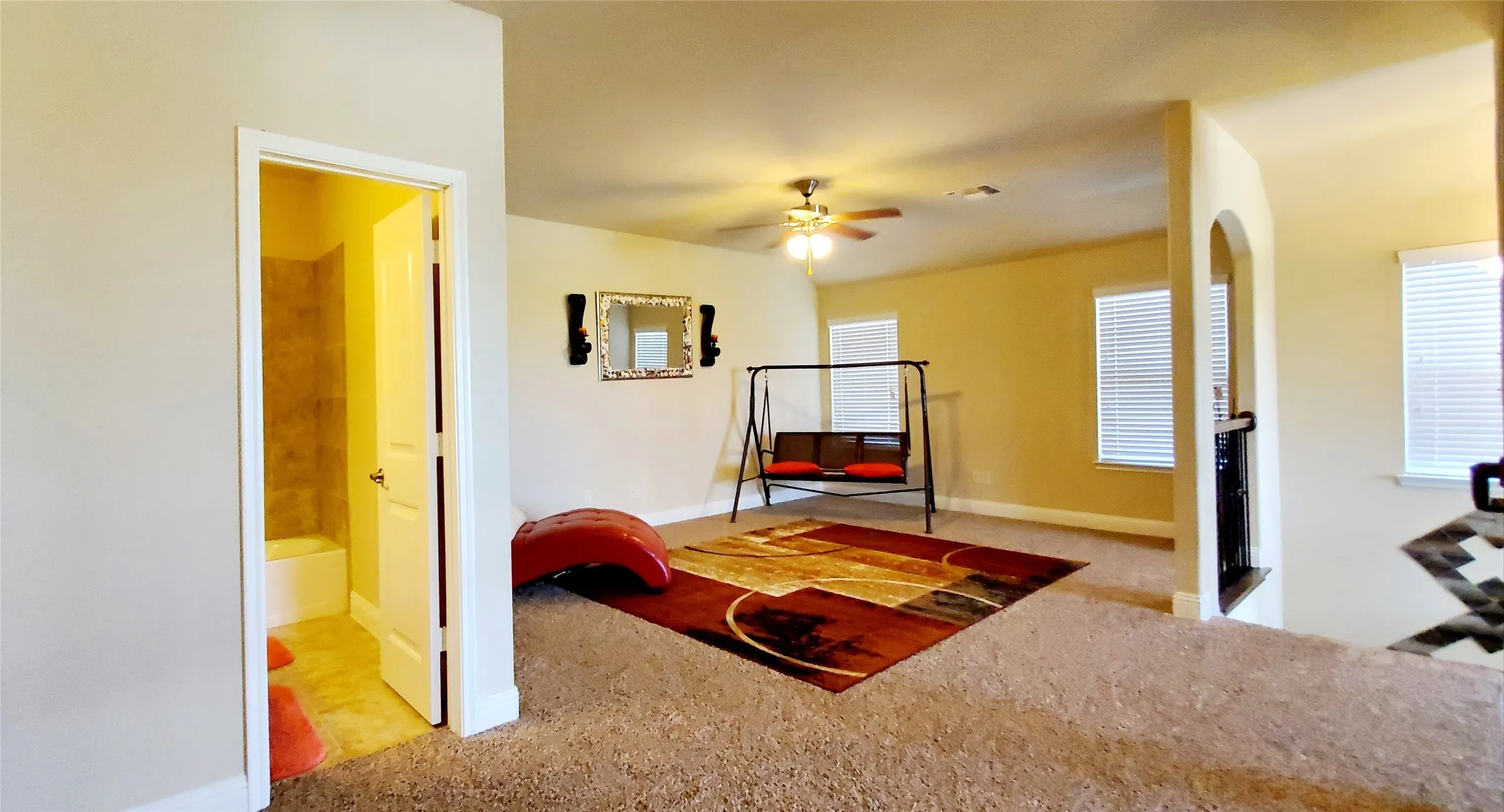 Carpeted upper-level space featuring a ceiling fan, multiple windows with blinds, an arched doorway, and an adjacent bathroom with a tub/shower combination