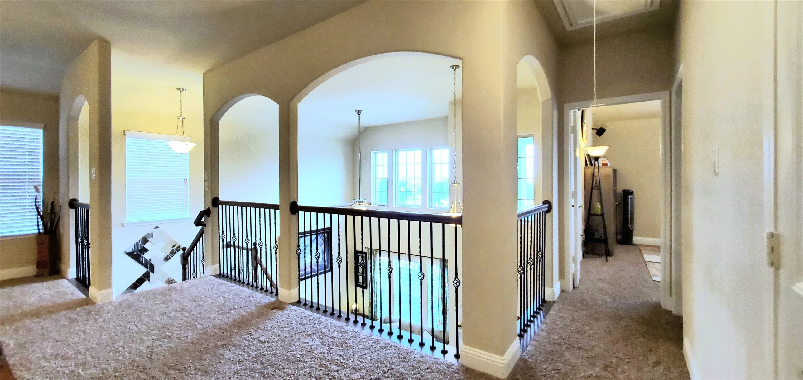Upper-level landing featuring neutral carpeting, arched doorways, and wrought iron balusters