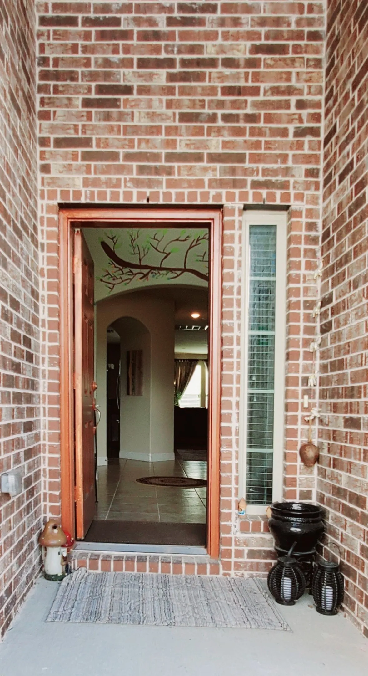 Brick exterior entrance with a solid wood door, sidelight window, and tiled interior flooring