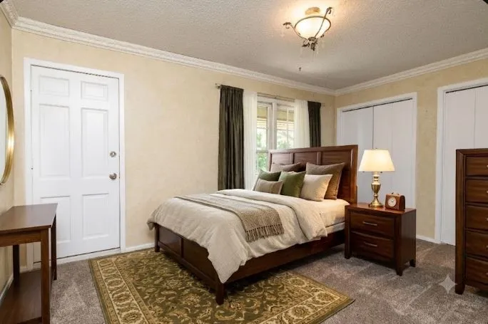 15.4 x 10.8 Upstairs Carpeted bed room featuring a white paneled door, two white bifold closet doors, a window with curtains, and crown molding with outside door to the front balcony