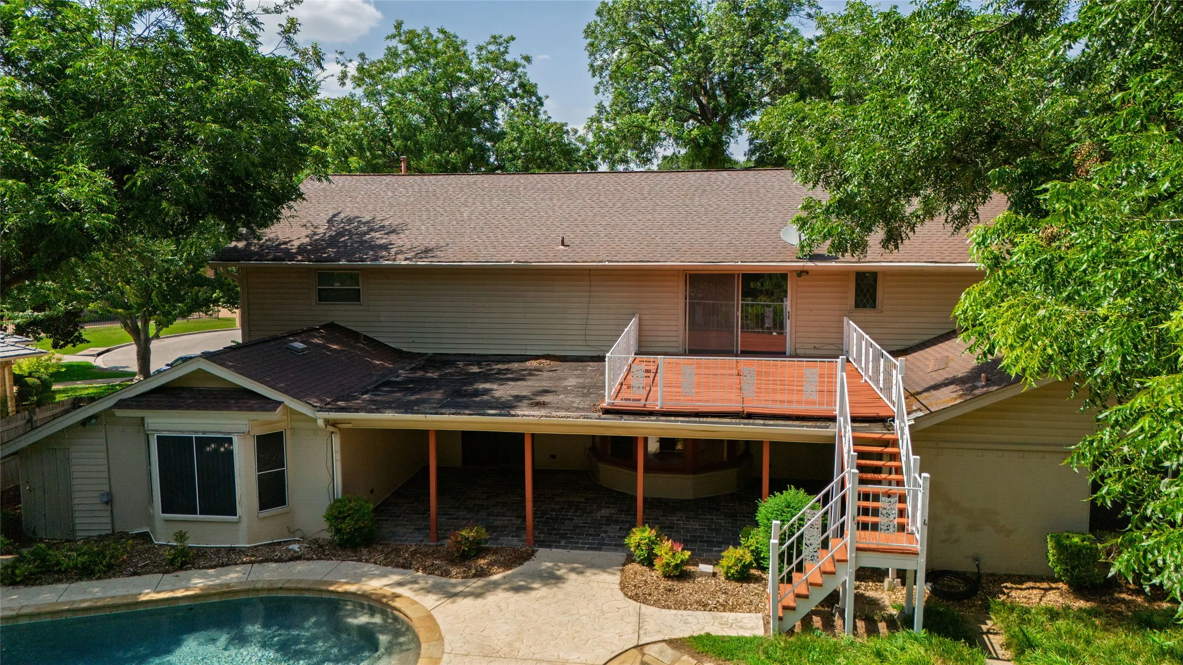 Rear facade featuring a second-story deck with white railings, a lower-level patio, and a concrete-surrounded swimming pool