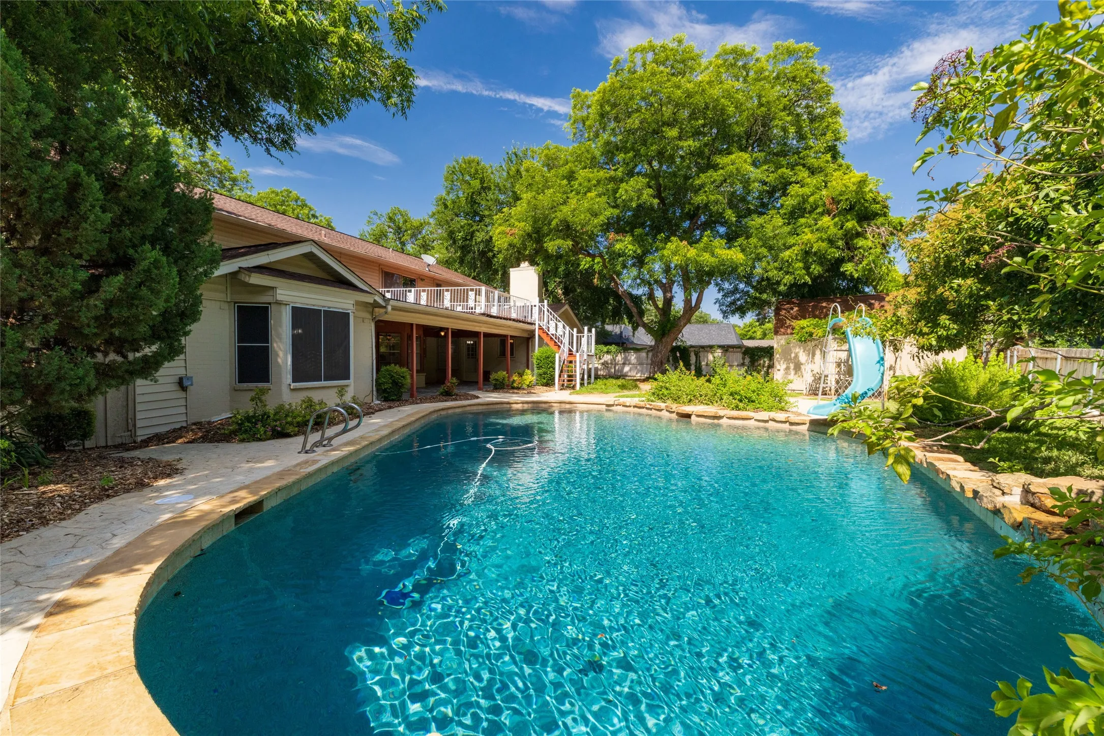 Curved swimming pool with stone coping and surrounding flagstone patio