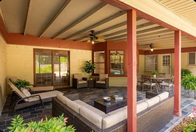 Spacious 33.4 x 16.3 covered patio featuring slate-style tile flooring, exposed beam ceiling with integrated ceiling fans, and direct access to the interior living via glass doors and a white paneled door into gameroom
