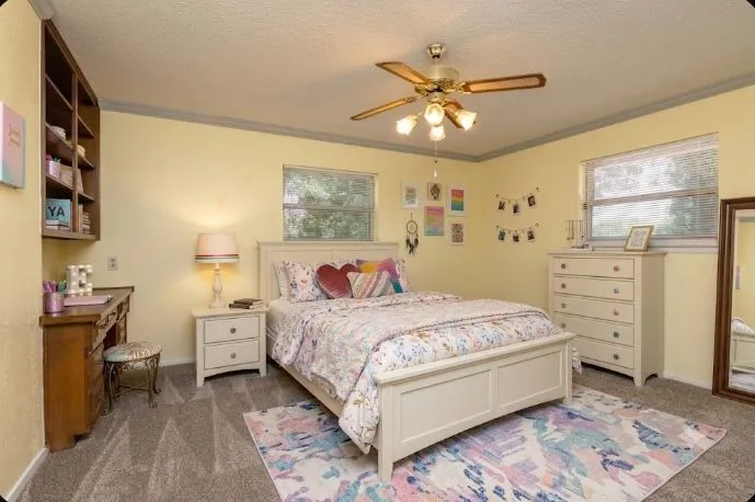 14 x 15.4 Spacious upstairs bedroom featuring carpet flooring, built-in shelving, two windows with blinds, a ceiling fan with integrated lighting,