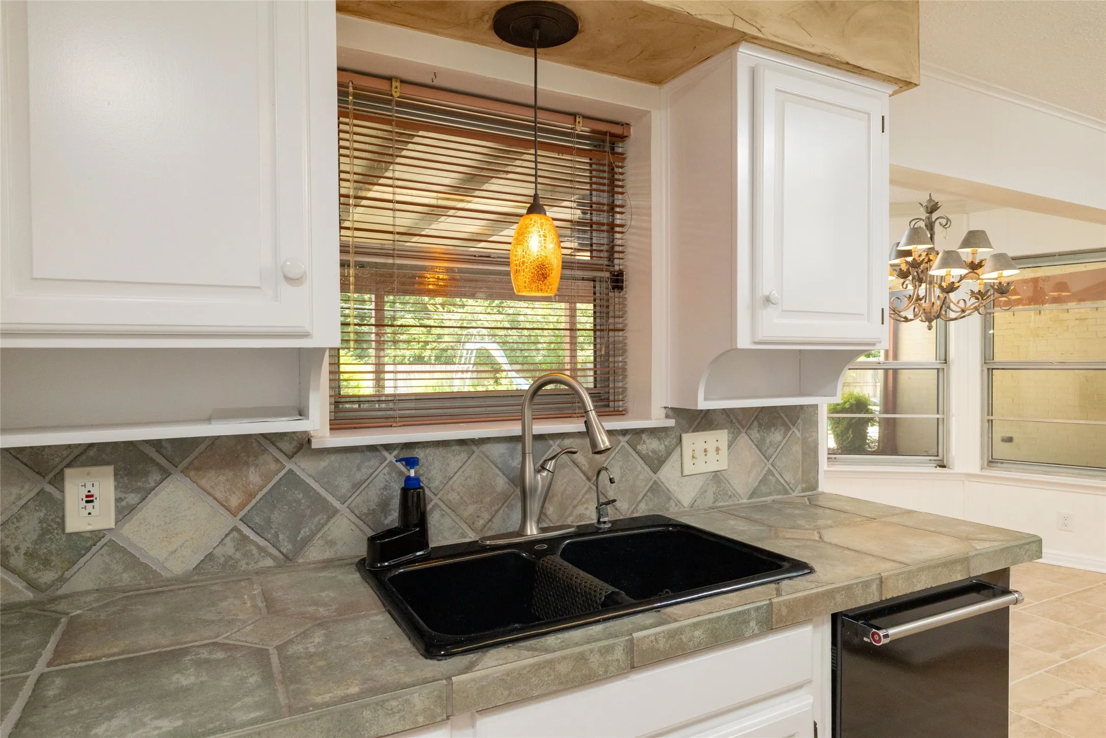 Kitchen sink area featuring a black double basin sink with a gooseneck faucet, tile countertops, and a complementary tile backsplash