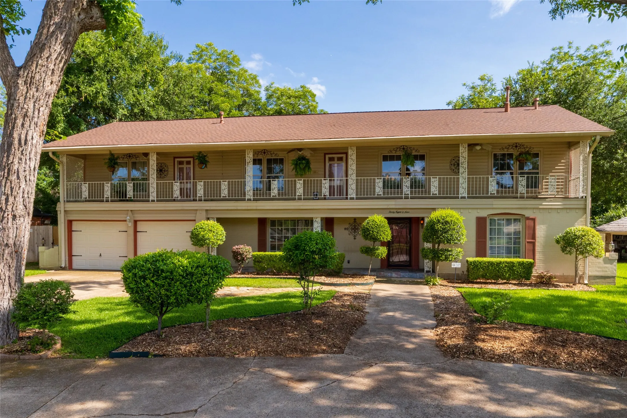 Two-story home with a New Orleans look featuring a full-width upper balcony with decorative railings, a two-car garage, and mature landscaping