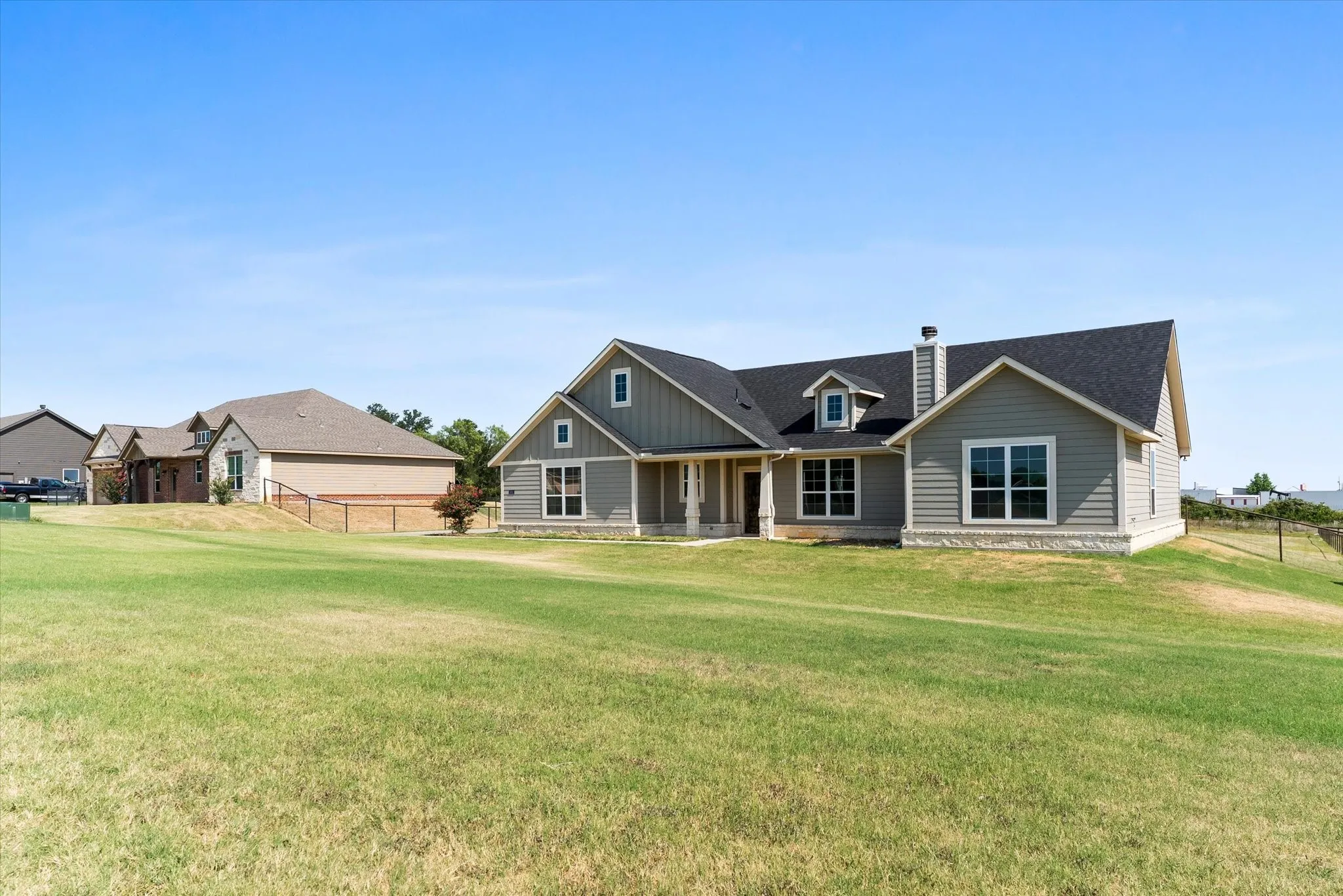 Single-story residence featuring light gray siding, dark shingle roof, stone accenting, and multiple dormer windows