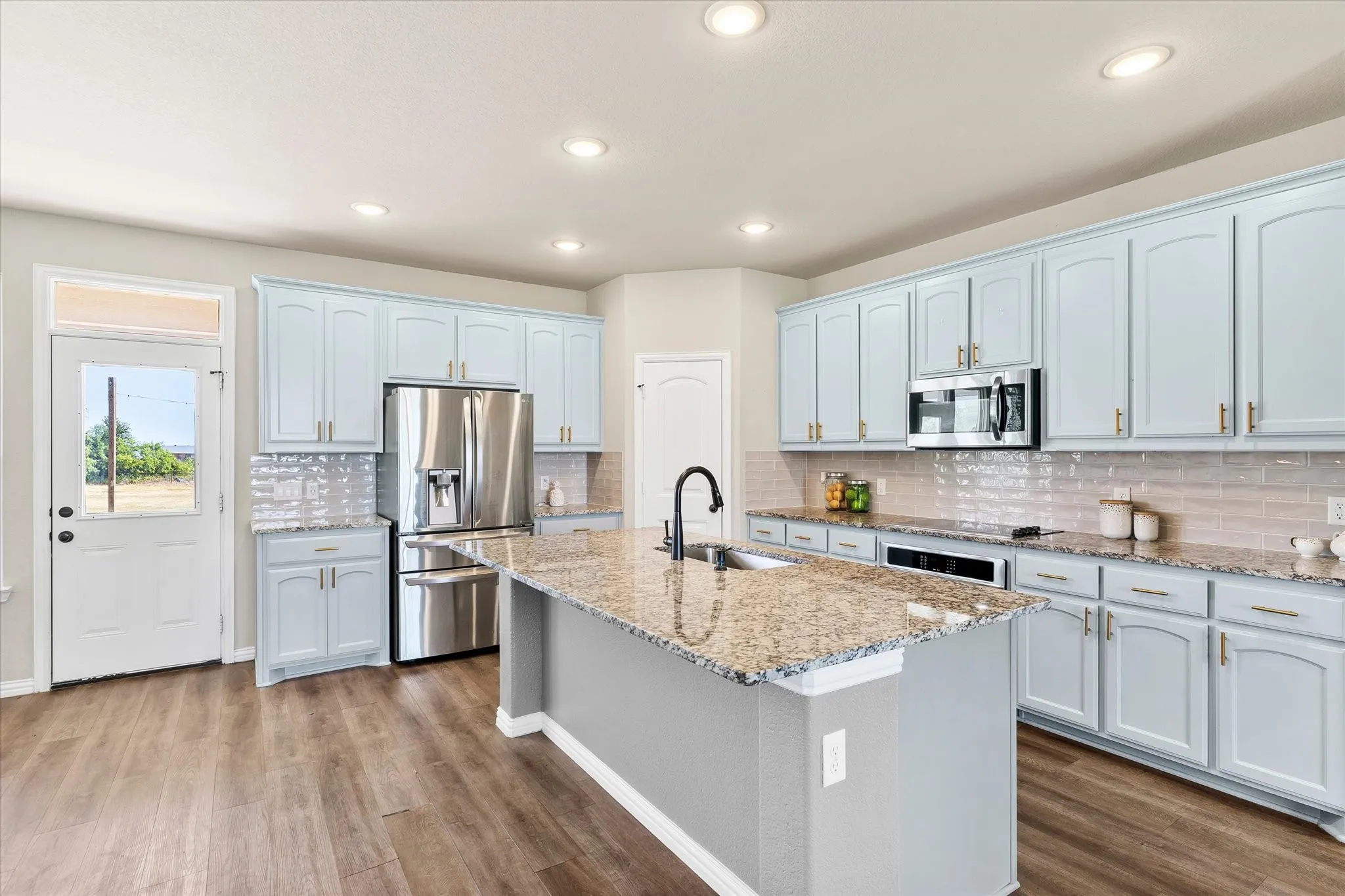 Elegant kitchen featuring light blue cabinetry, granite countertops, a large island with waterfall edge, stainless steel appliances including a French-door refrigerator, and subway tile backsplash