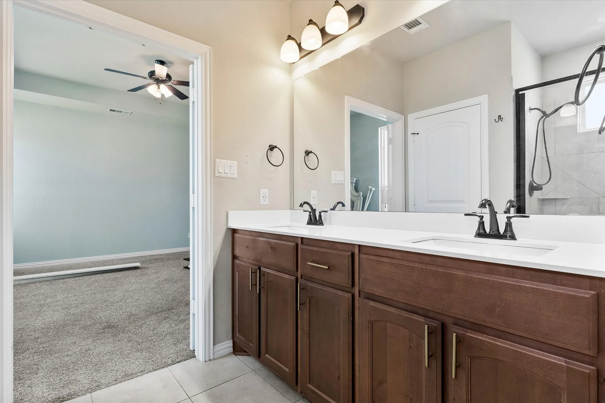 Dual vanity with wood-finish cabinetry, white countertops, and matte black fixtures