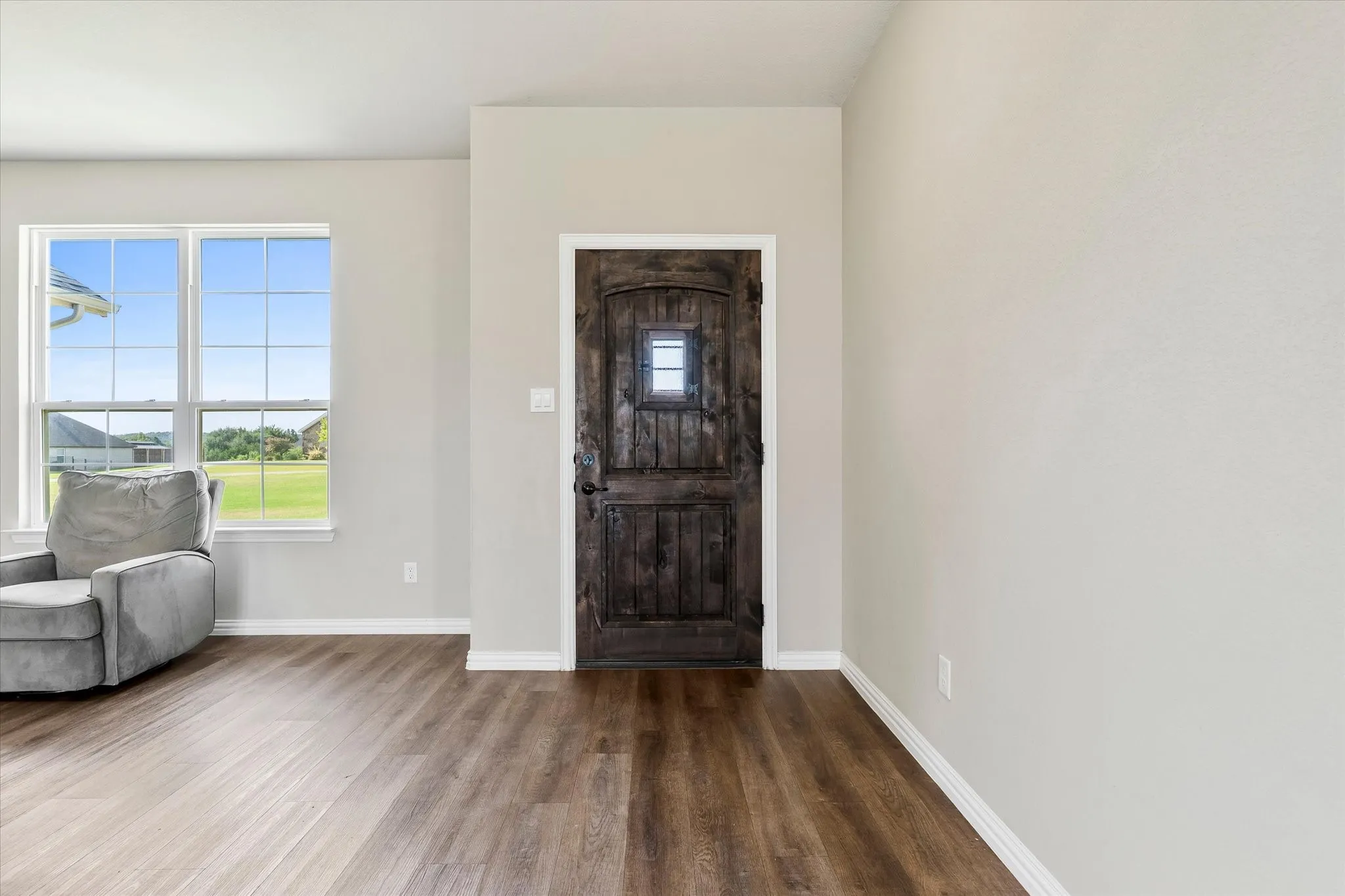 Wood-finish flooring, white trim, and a dark-stained entry door with a privacy window