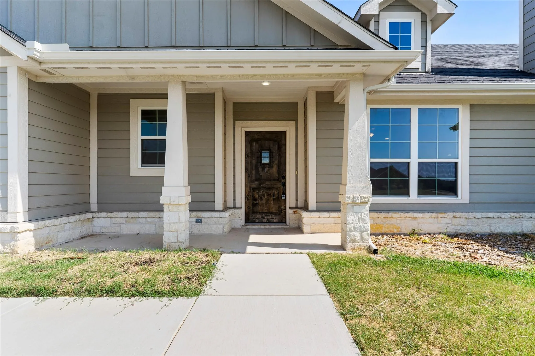Inviting covered porch with stone-based columns and wood-textured entry door