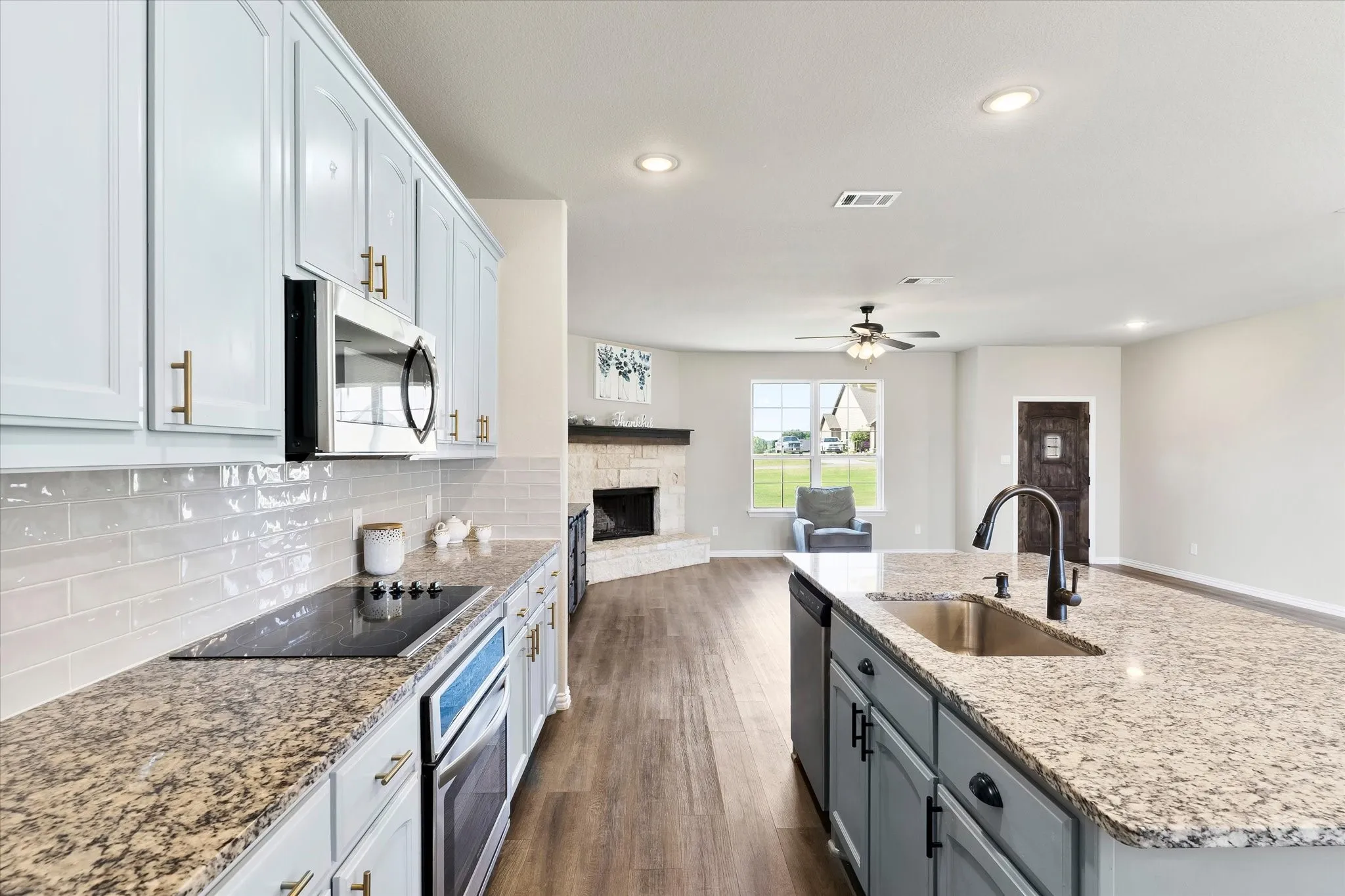 Granite countertops, subway tile backsplash, wood-finish flooring, built-in microwave, and a stone-faced fireplace