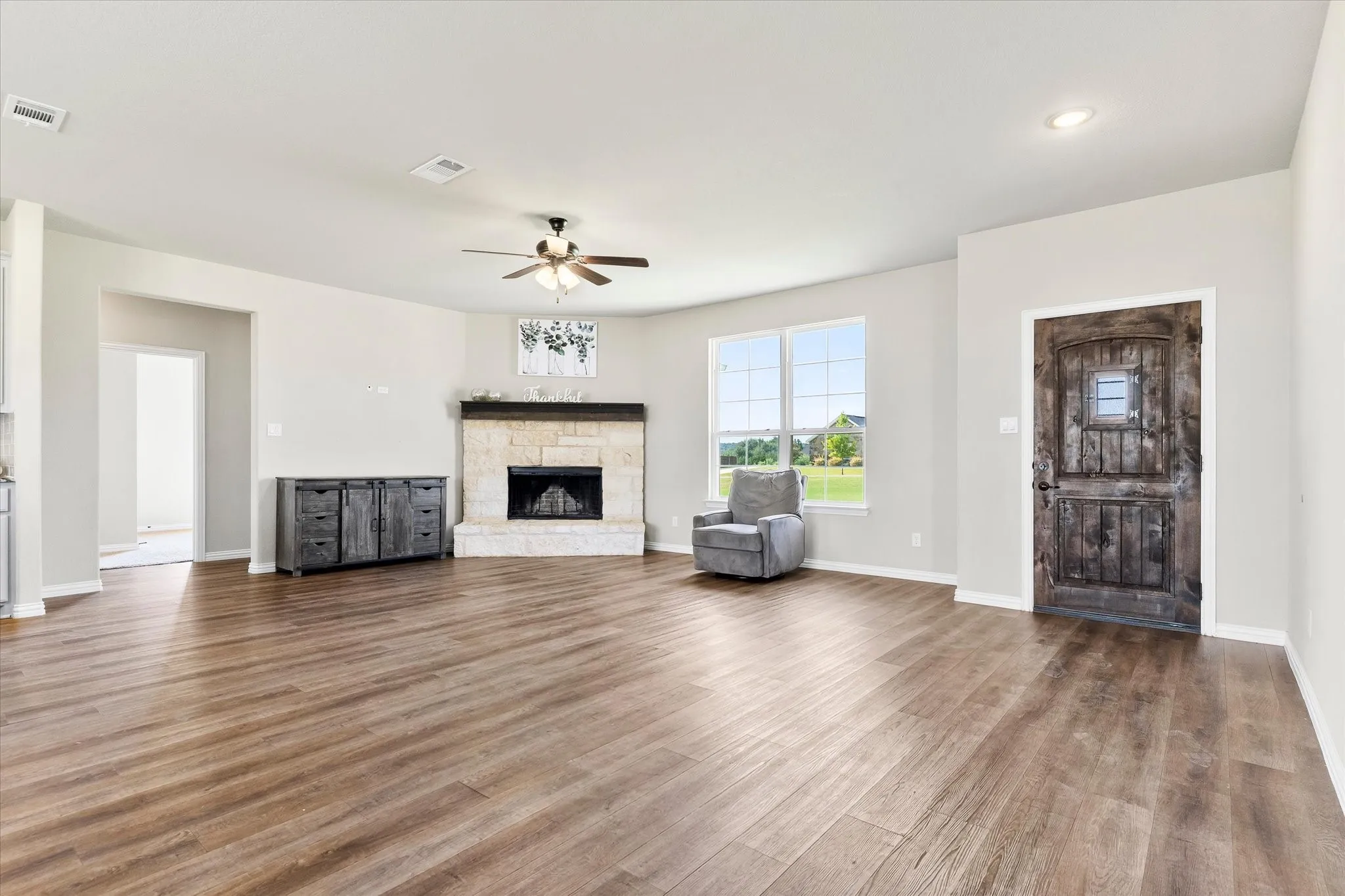 Spacious living area featuring wood-finish flooring, a stone-surround fireplace with a wood mantle, and a ceiling fan