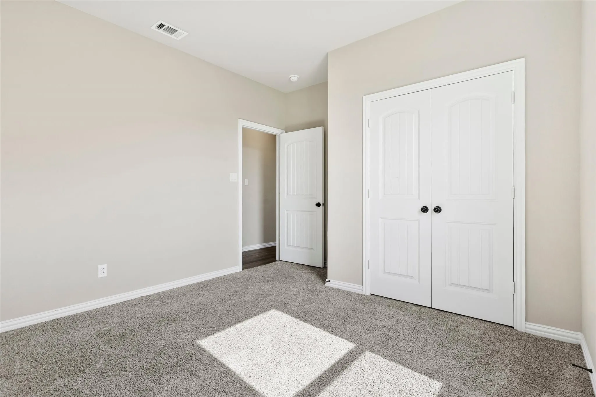 Plush carpet flooring, white trim, light neutral wall paint, white paneled bifold closet doors, and a white paneled interior door with a black handle