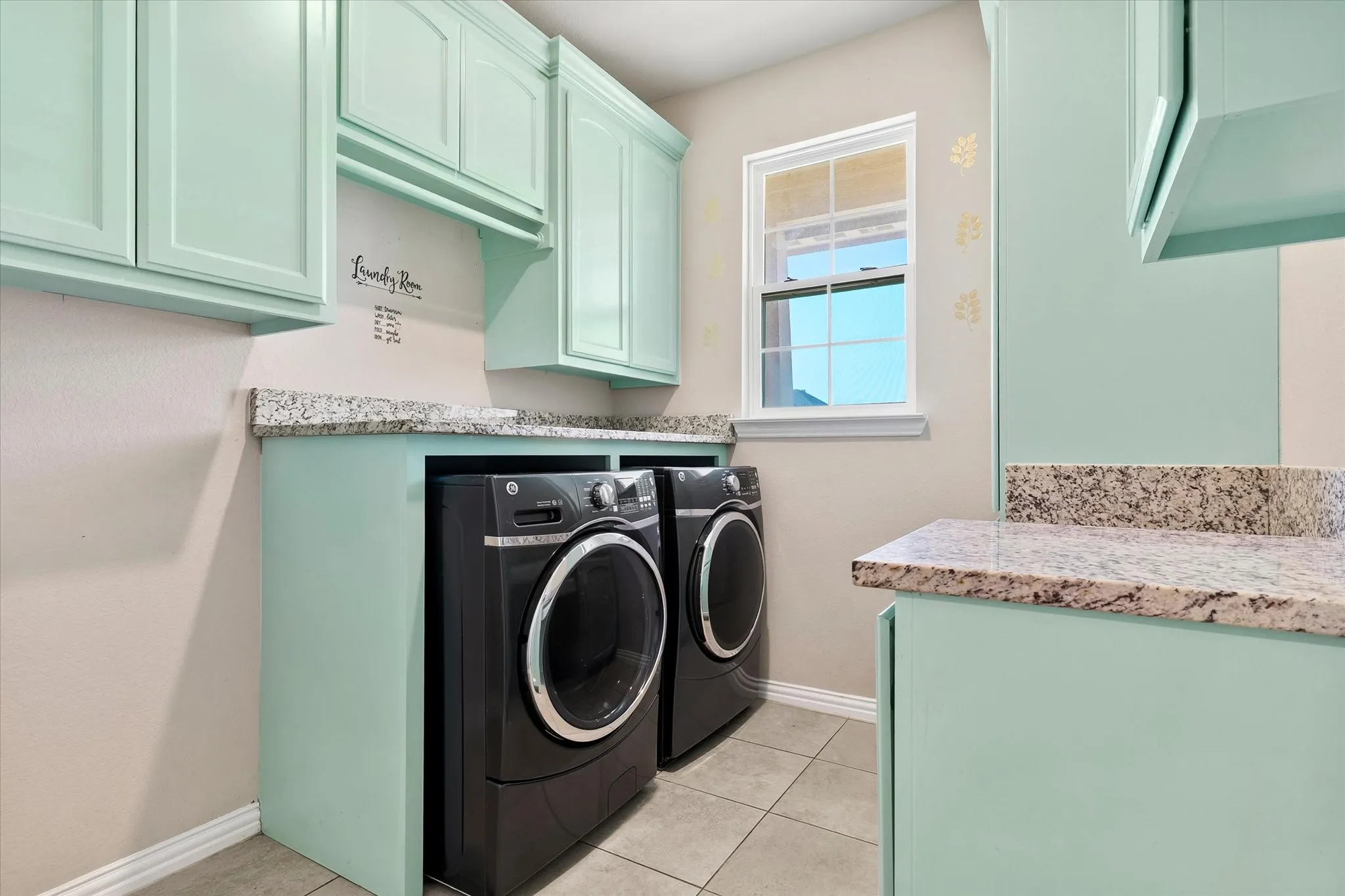 Mint green cabinetry with ample storage, speckled countertops, and tile flooring