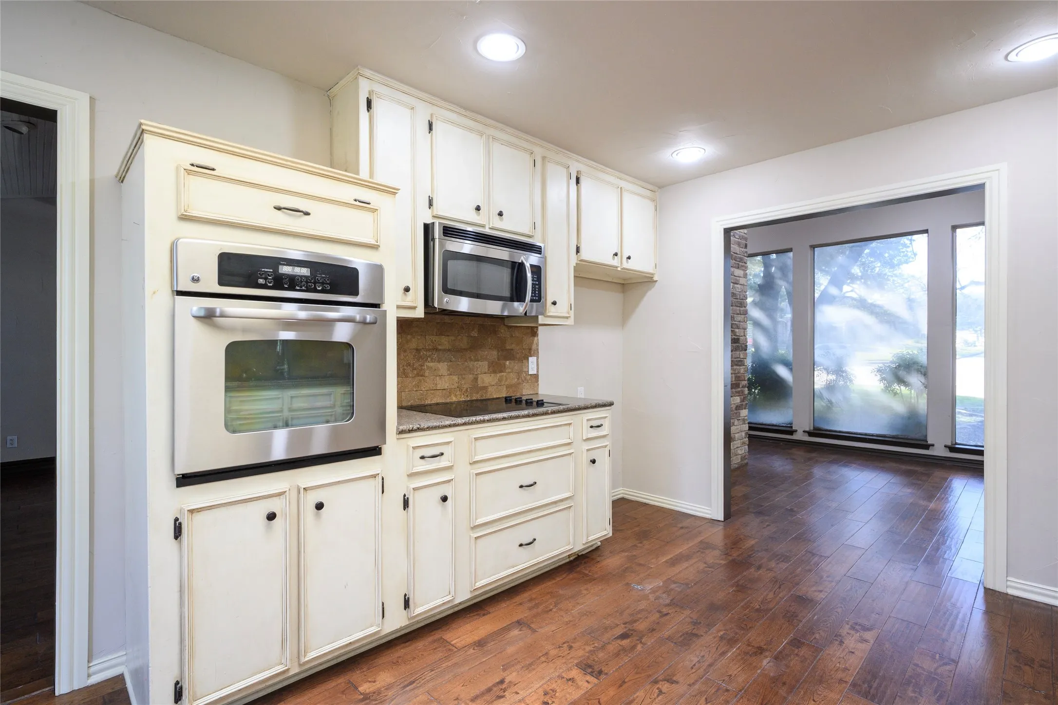 Kitchen featuring white cabinetry with dark hardware, stainless steel built-in oven, stainless steel microwave, stone tile backsplash, and wood-finish flooring