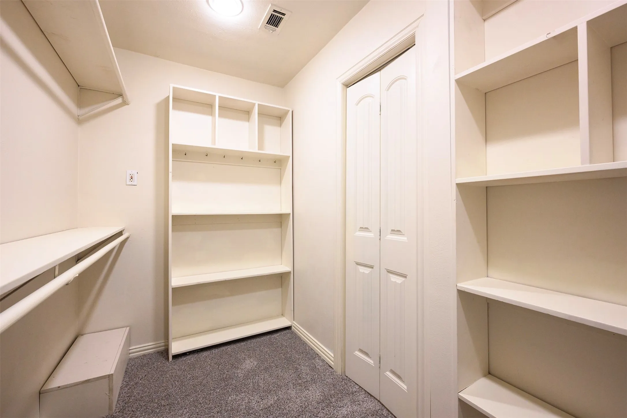 Closet featuring built-in shelving, hanging rod, neutral wall paint, gray carpet flooring, and a white bi-fold door
