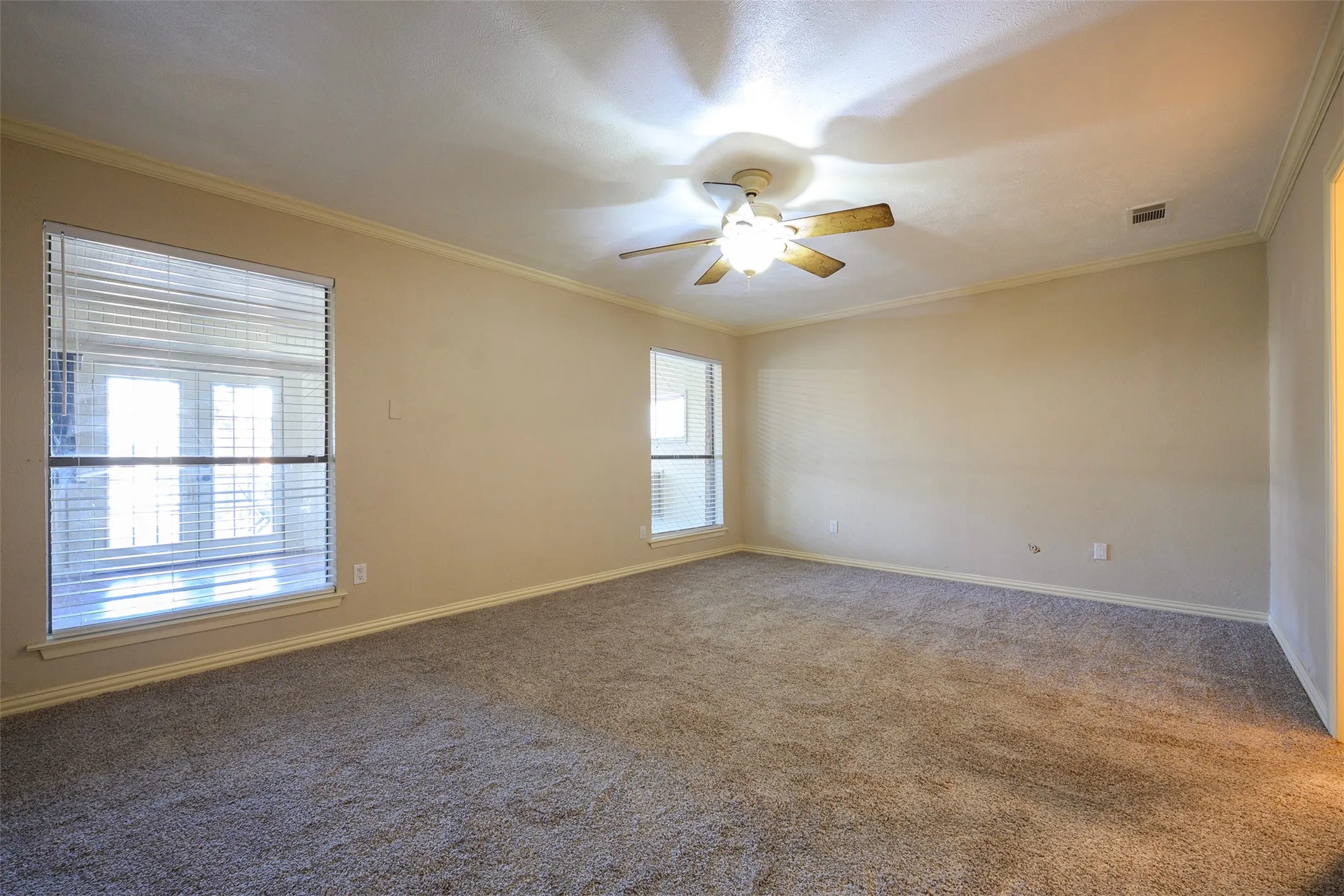 Spacious room featuring neutral carpeting, crown molding, and a ceiling fan with integrated lighting