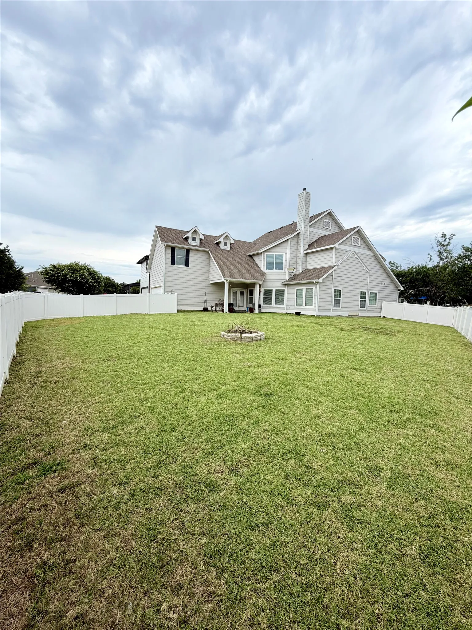 Spacious backyard featuring a large green lawn and a white privacy fence