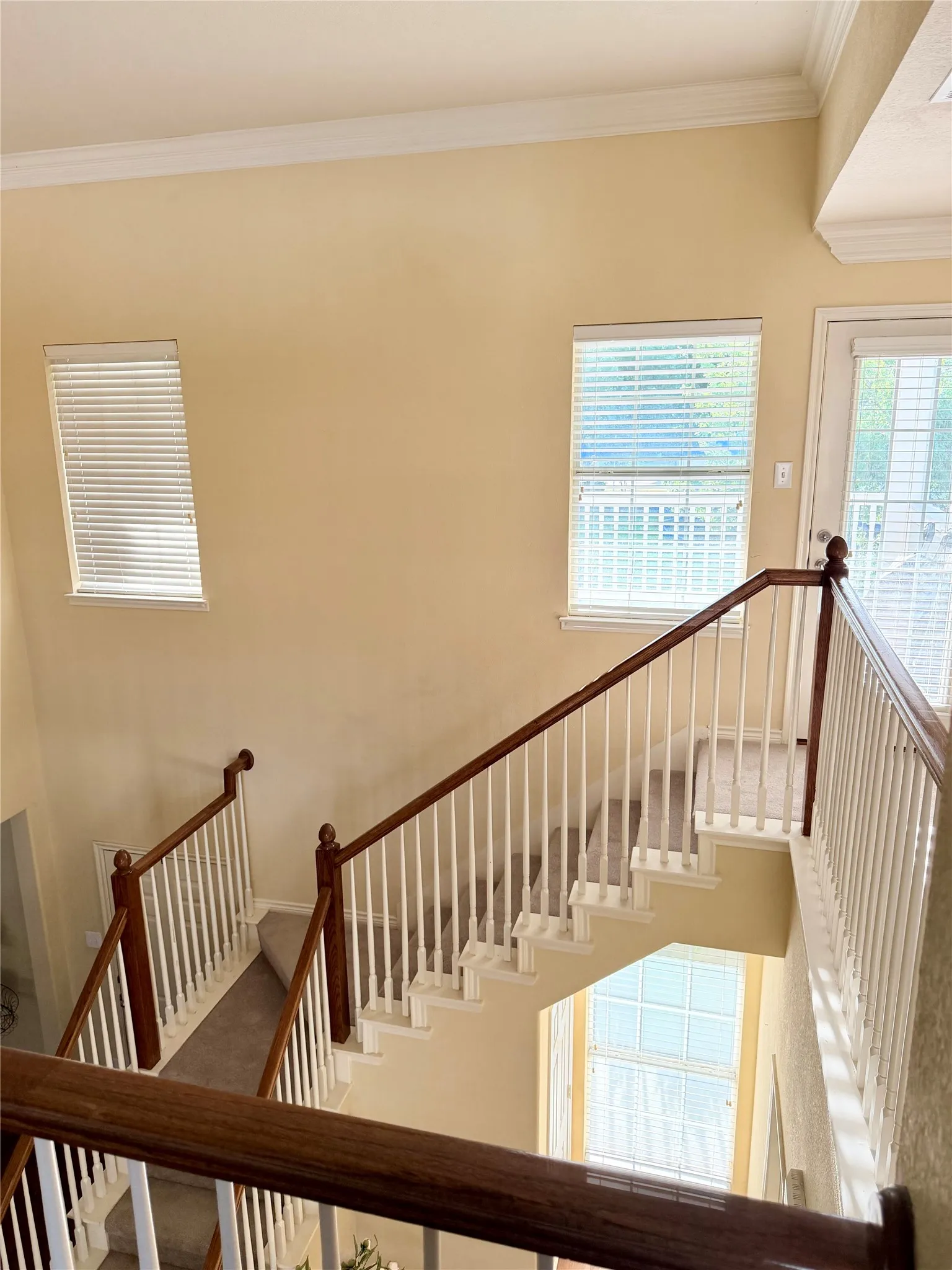 Two-story staircase featuring wood handrails, white spindles, and carpeted treads