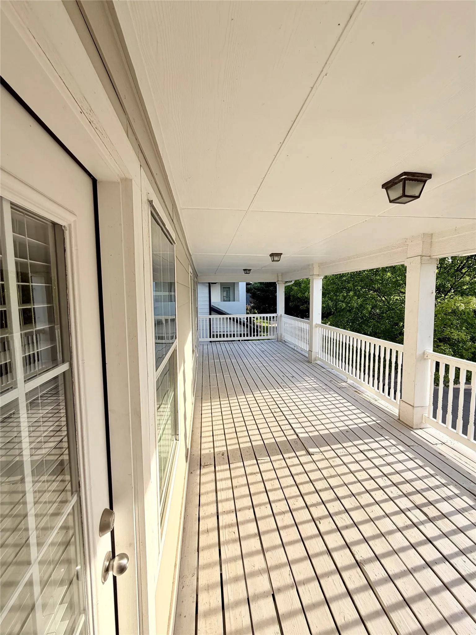 Expansive covered second floor porch featuring a painted wood-finish floor, white spindle railing, recessed lighting, and multiple windows with grids