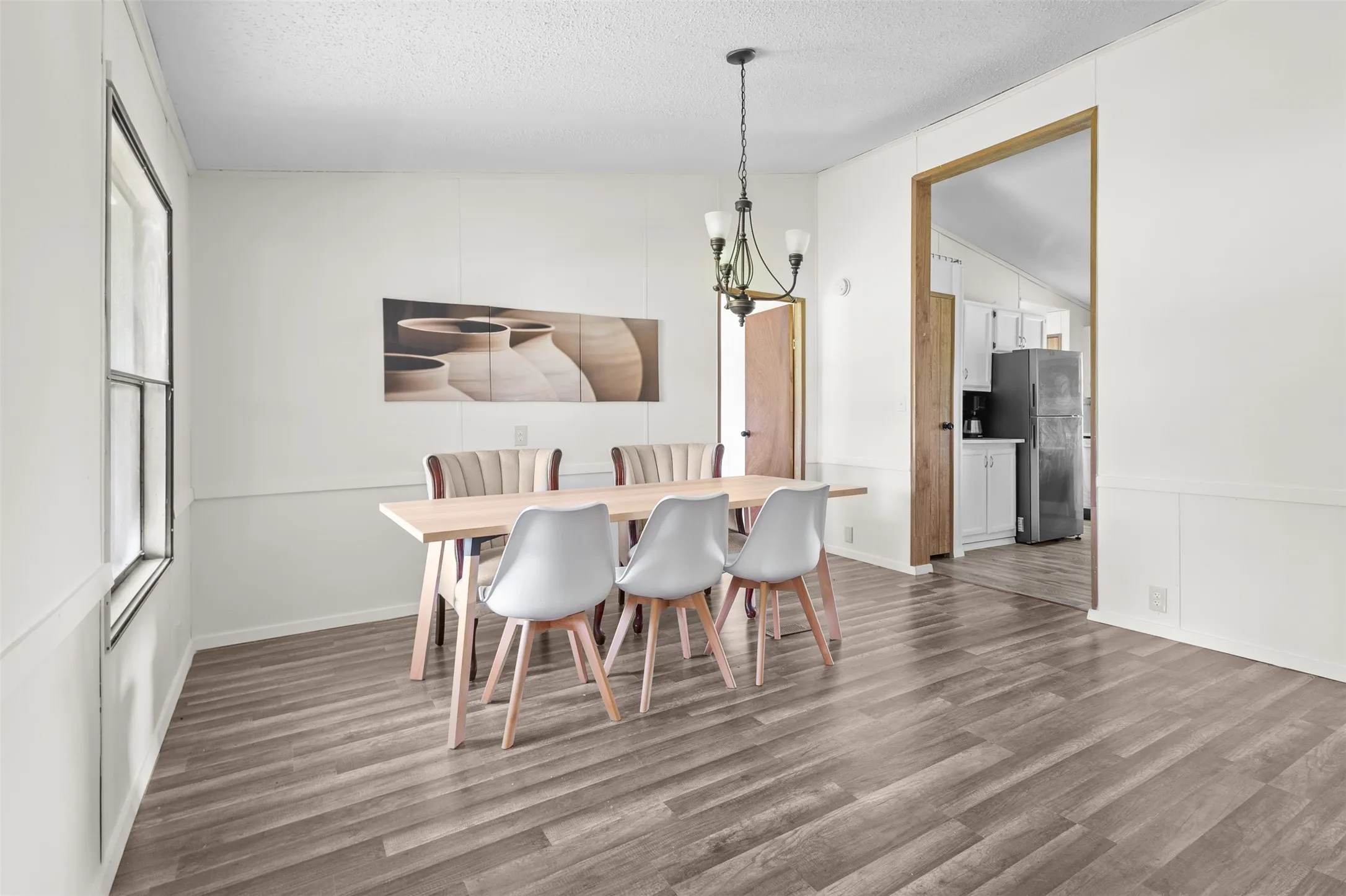 Dining area featuring wood-finish flooring, white paneling, and an overhead chandelier