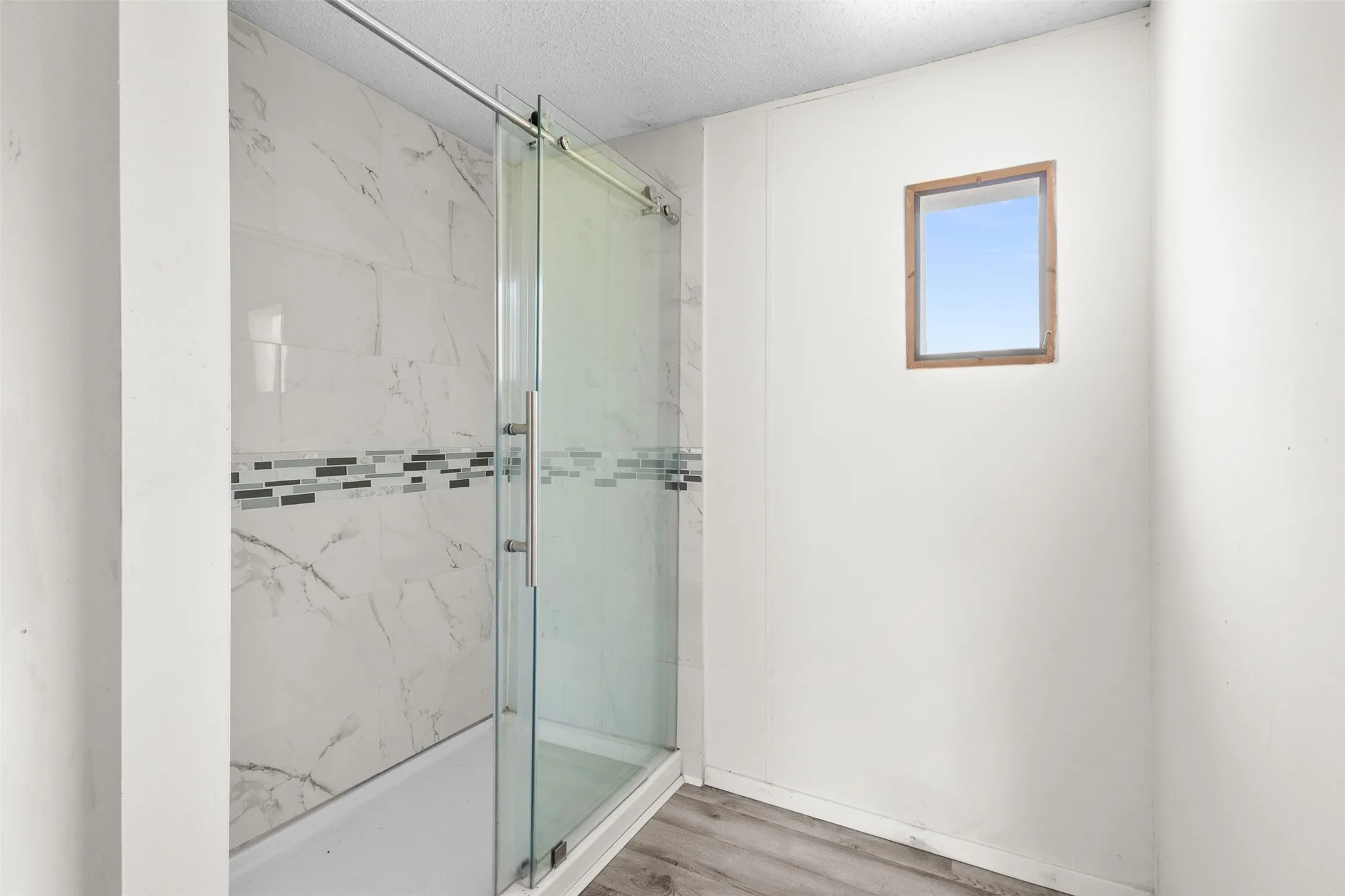 Shower enclosure featuring white marble-look tile, a decorative mosaic tile band, and a clear glass sliding door